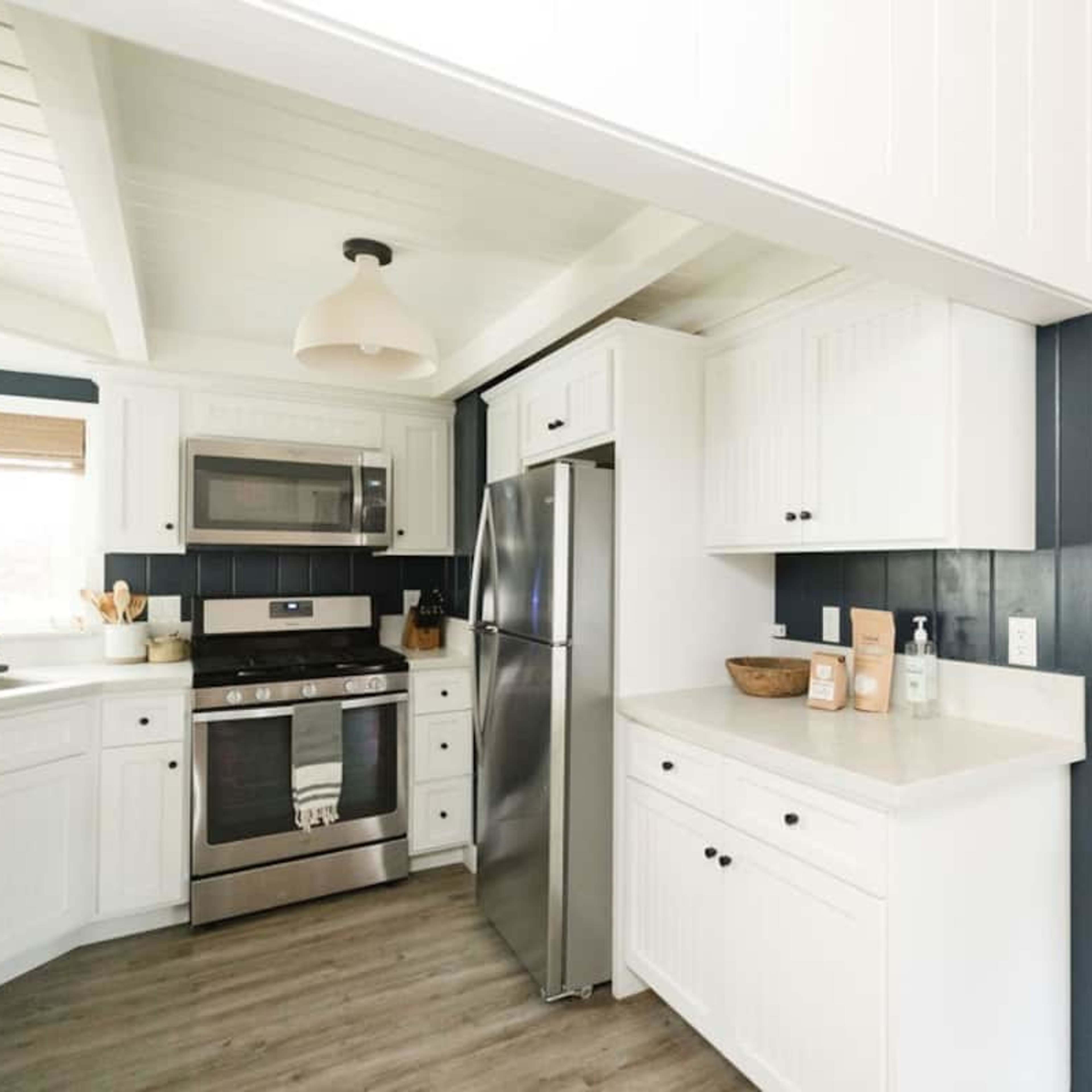 A modern kitchen with white wood cabinetry, stainless steel appliances, and a light-colored countertop.