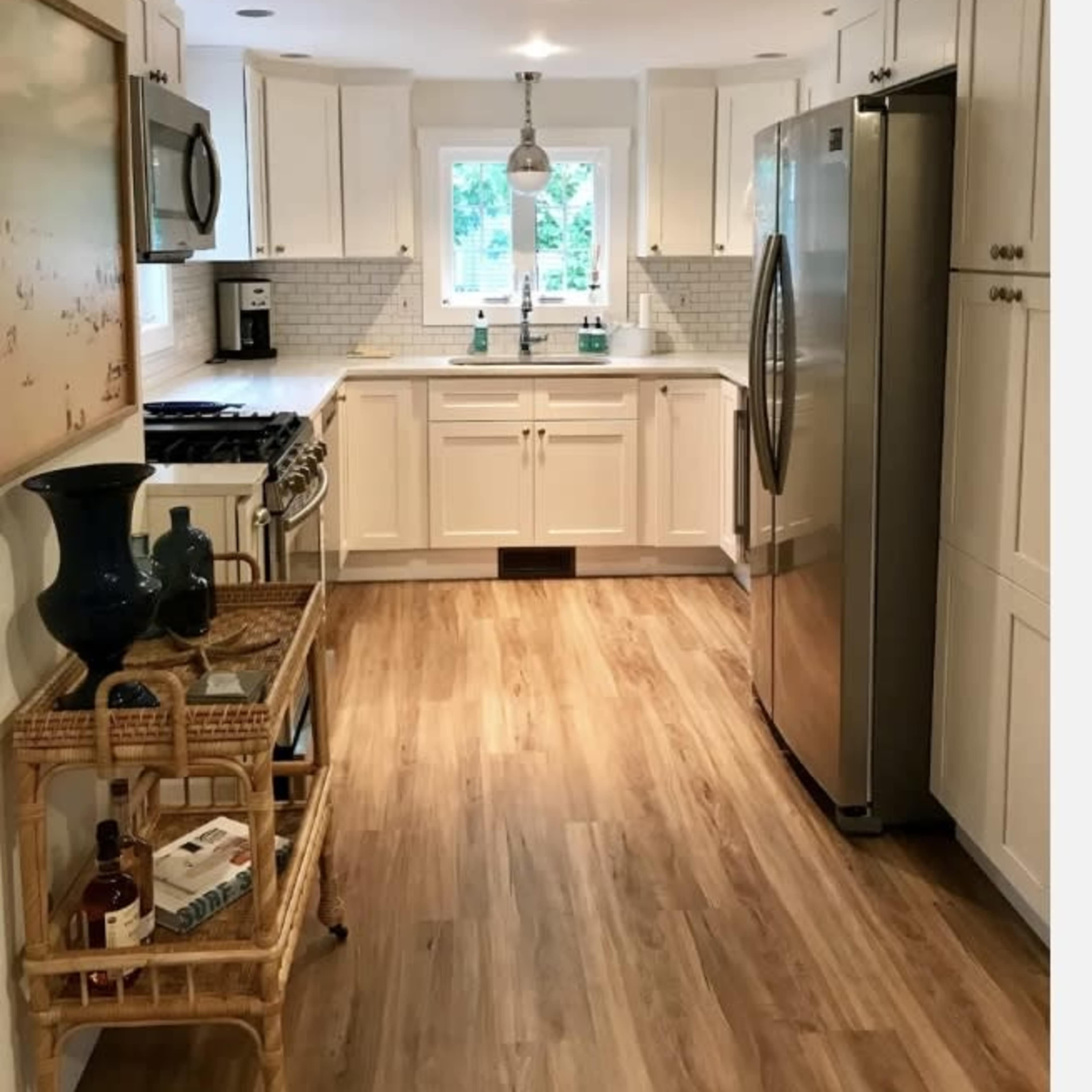 A modern kitchen with white cabinets, a stainless steel refrigerator, and a wooden floor.