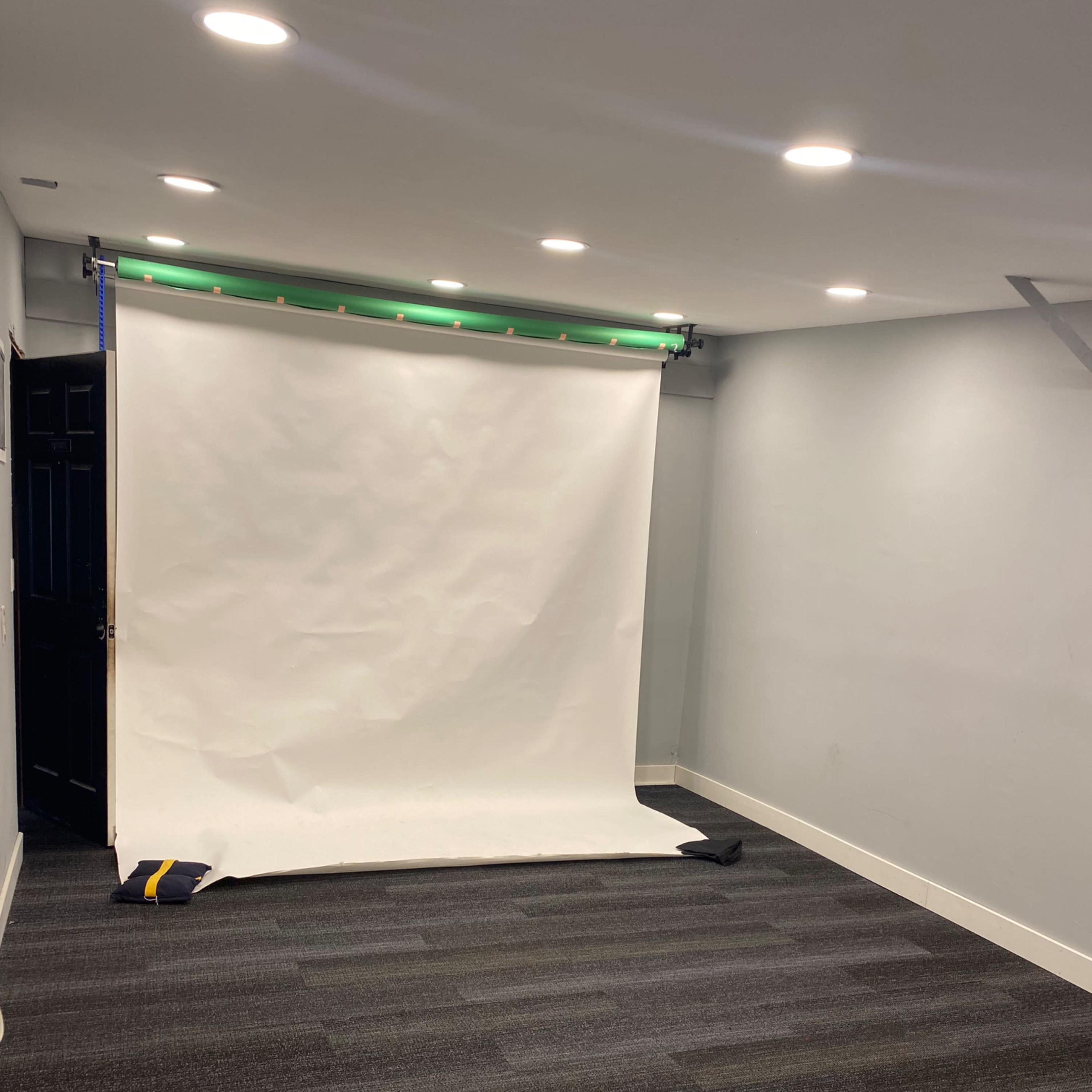 An empty room with a white backdrop set up and green lighting, along with a dark door and gray carpet.