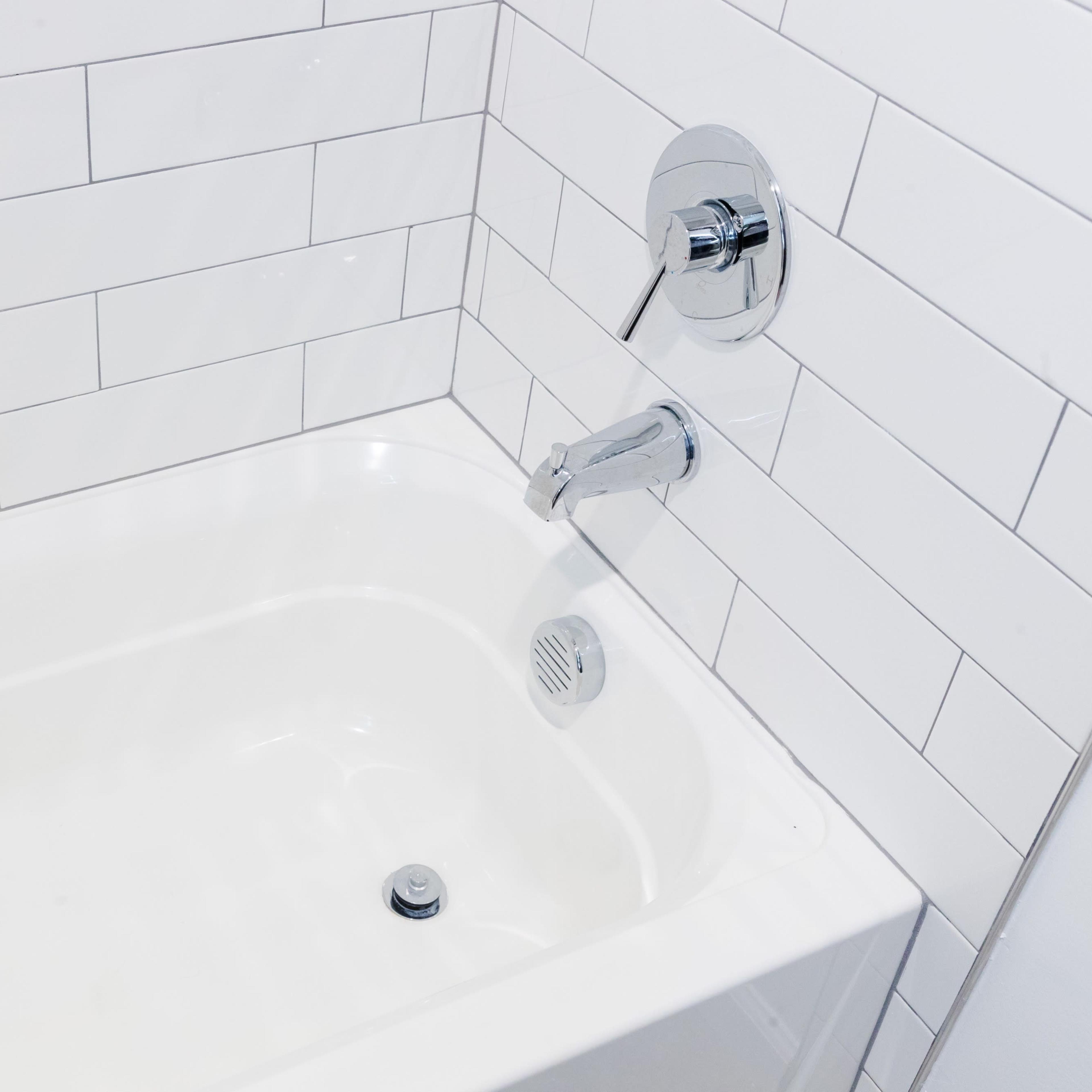 A white bathtub with chrome fixtures against a wall of white subway tiles.