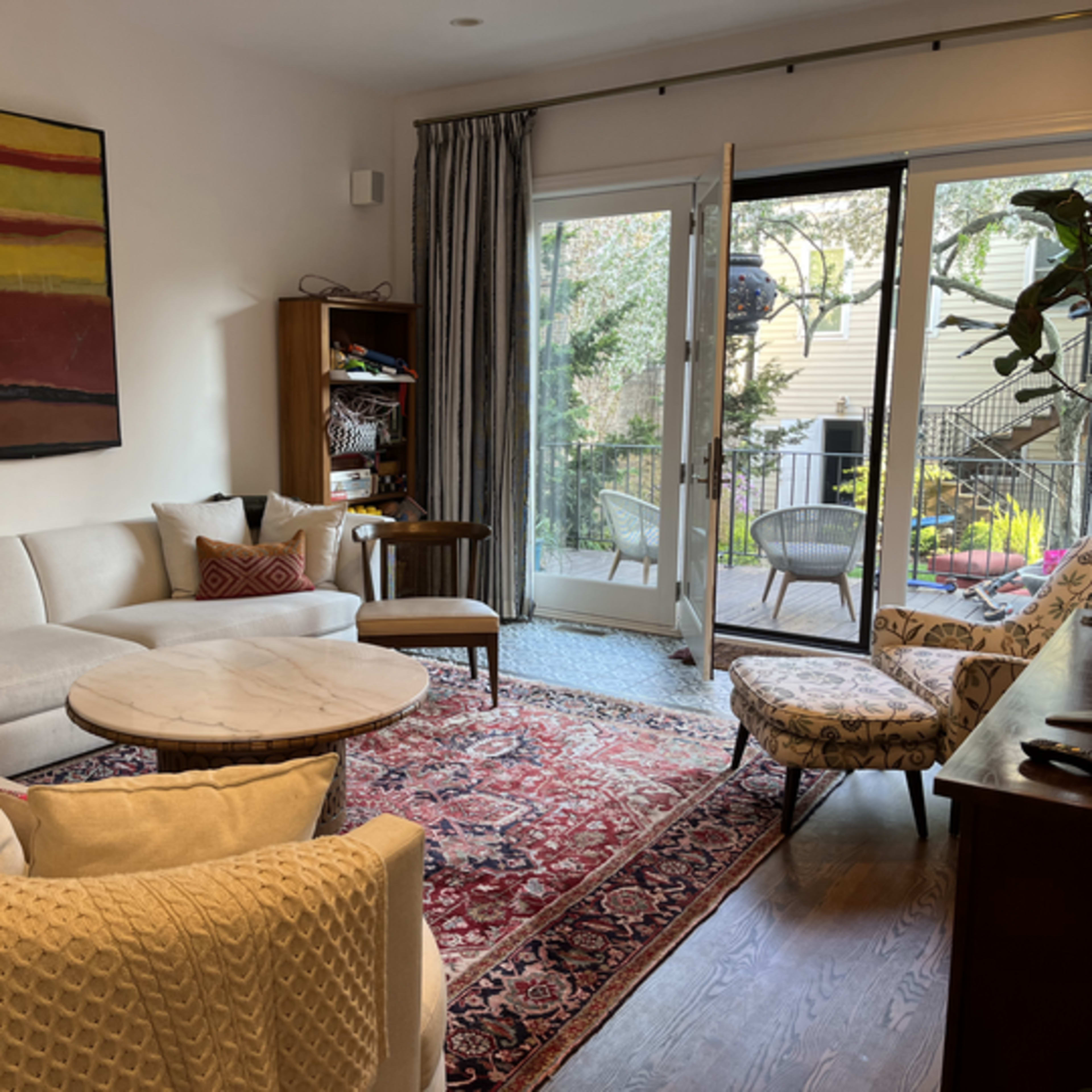 A living room features a sectional sofa, a round coffee table, a patterned rug, and large glass doors leading to a patio area with outdoor seating.