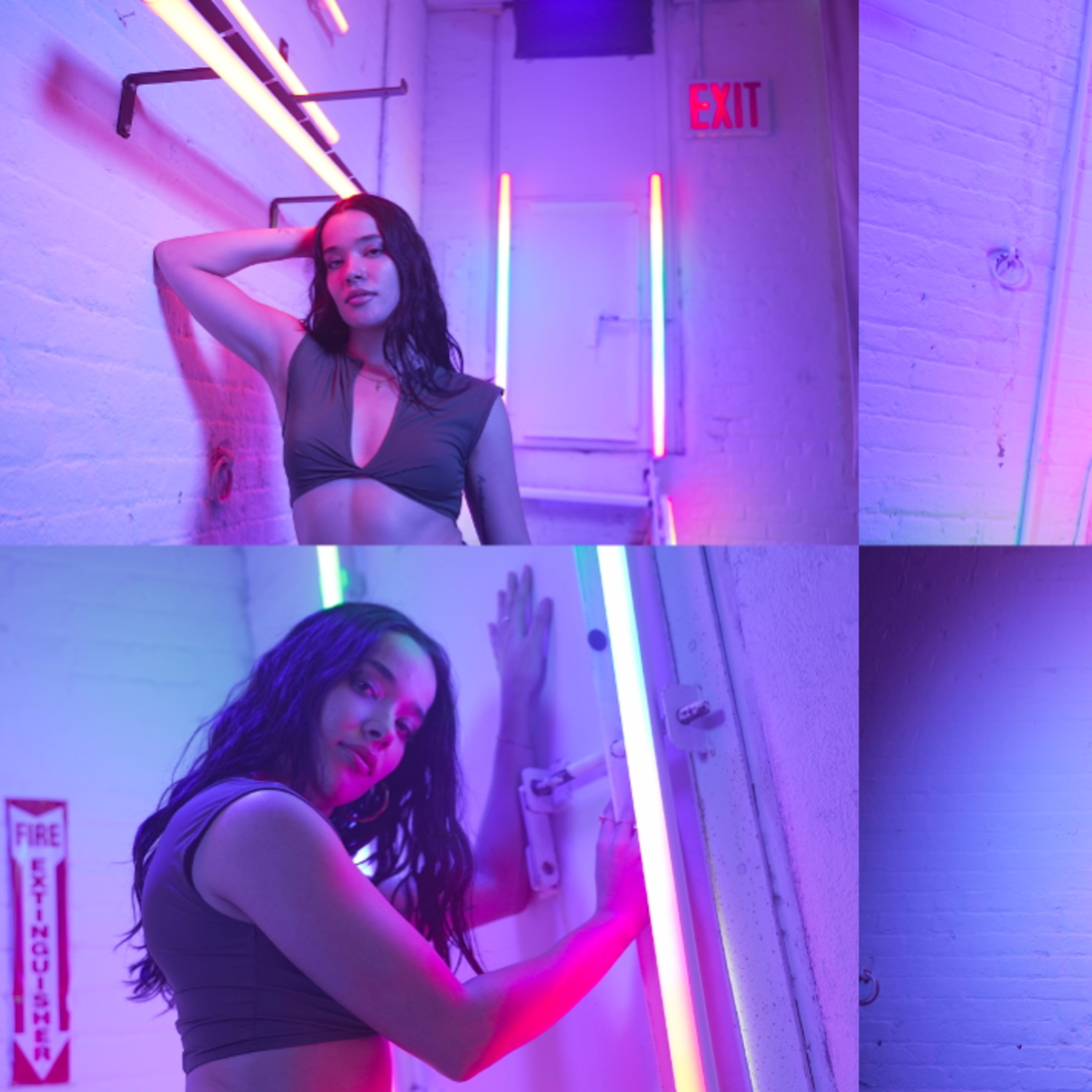 A model posing in a neon-lit corridor with colorful lighting effects against a white brick wall.