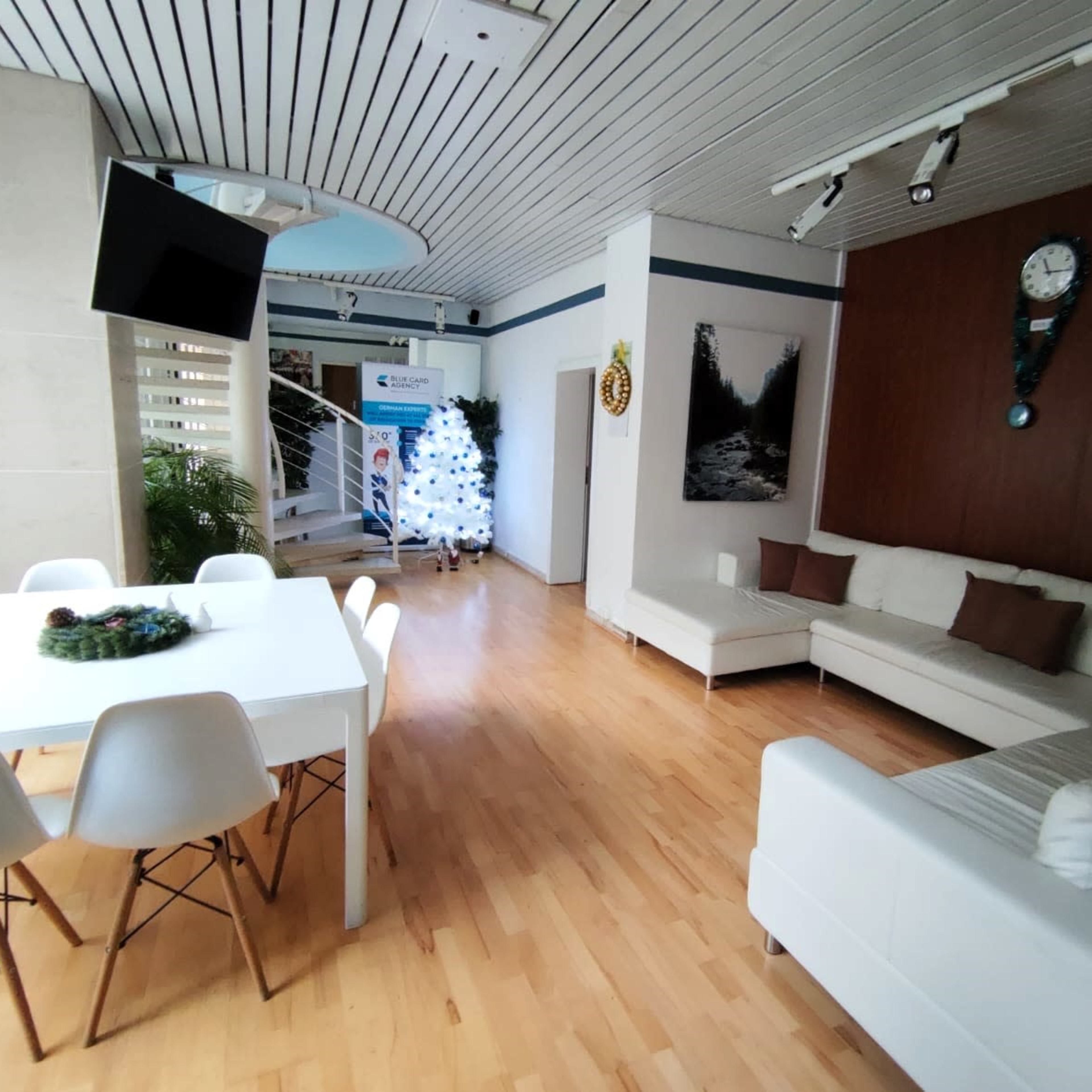 A modern interior space features a white sofa, a dining table with chairs, and a Christmas tree in the corner, with a staircase in the background.