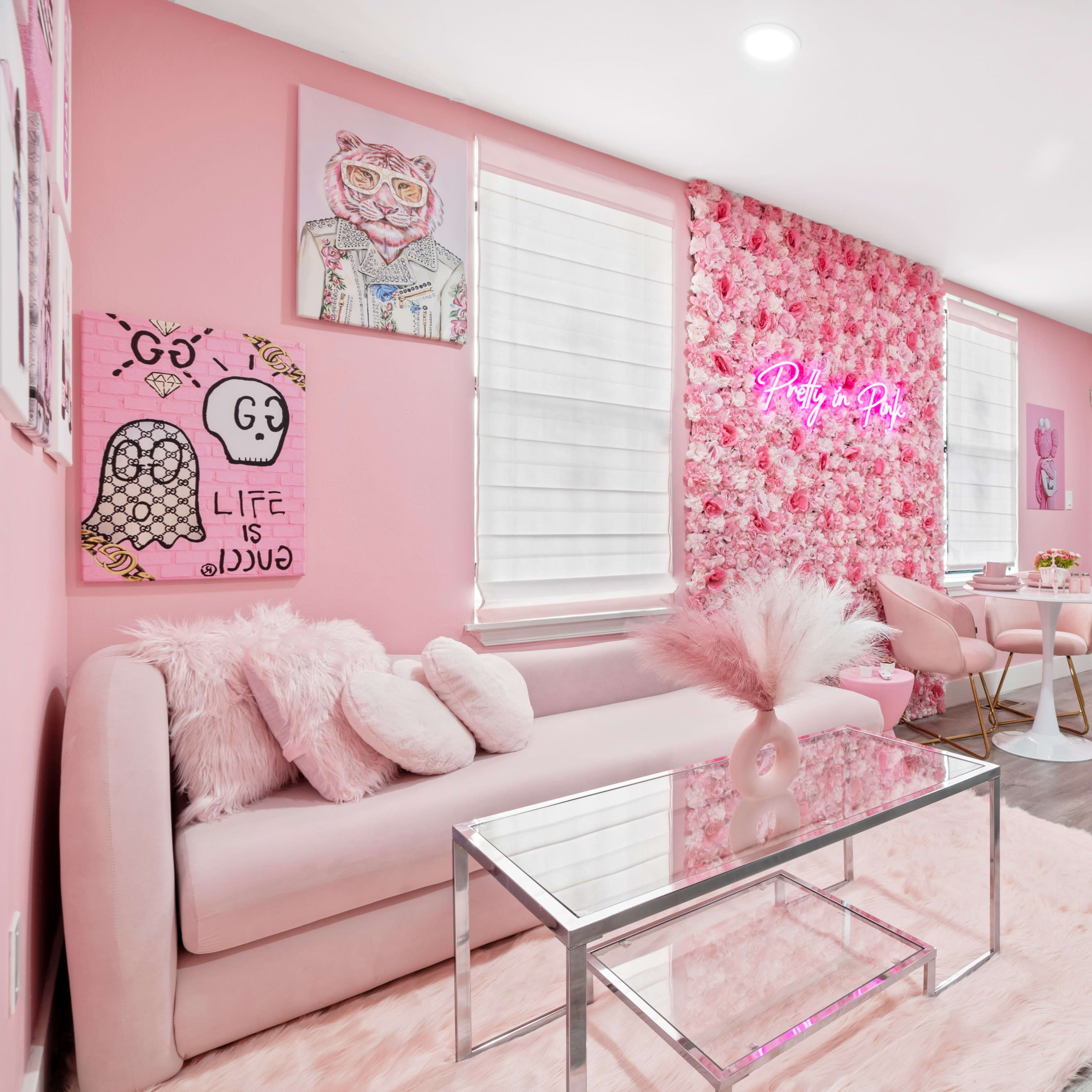 A bright pink-themed kitchen and living area featuring a floral accent wall, a glass coffee table, and modern furniture.