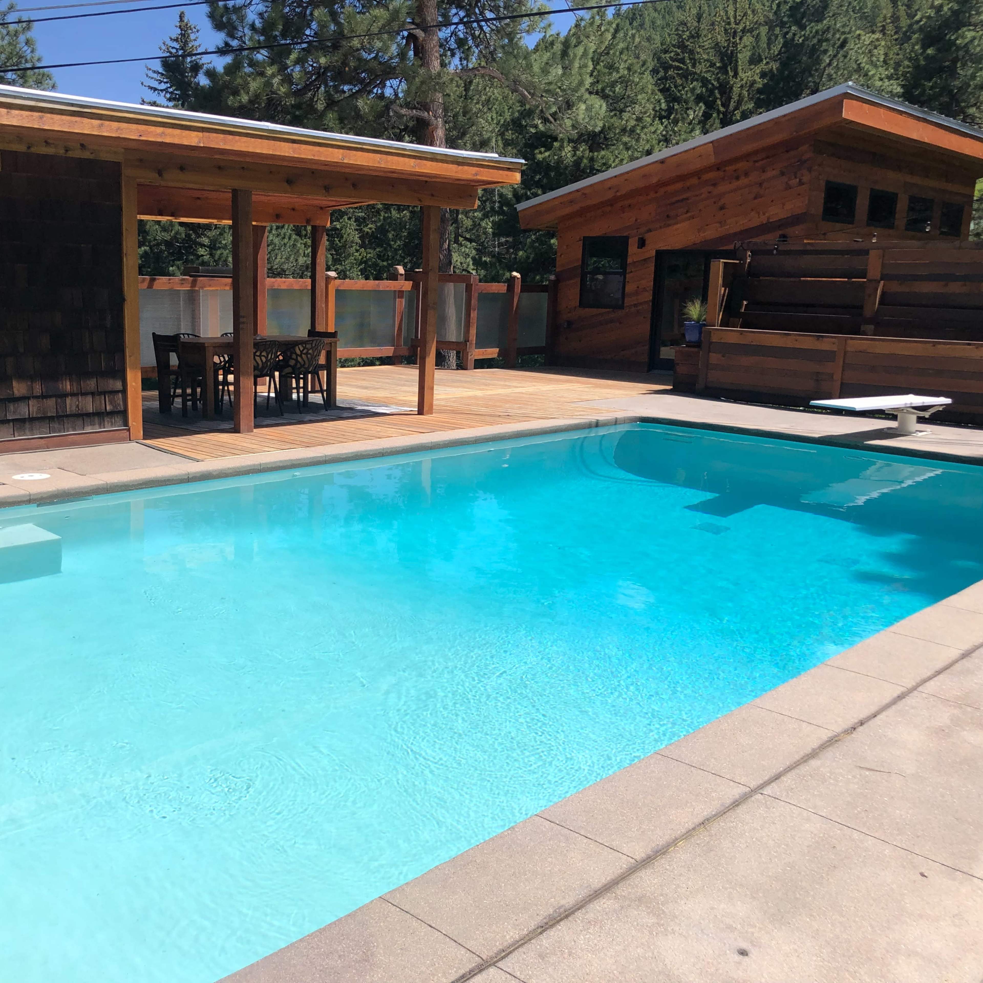 A clear swimming pool surrounded by wooden structures and a deck area with outdoor seating.