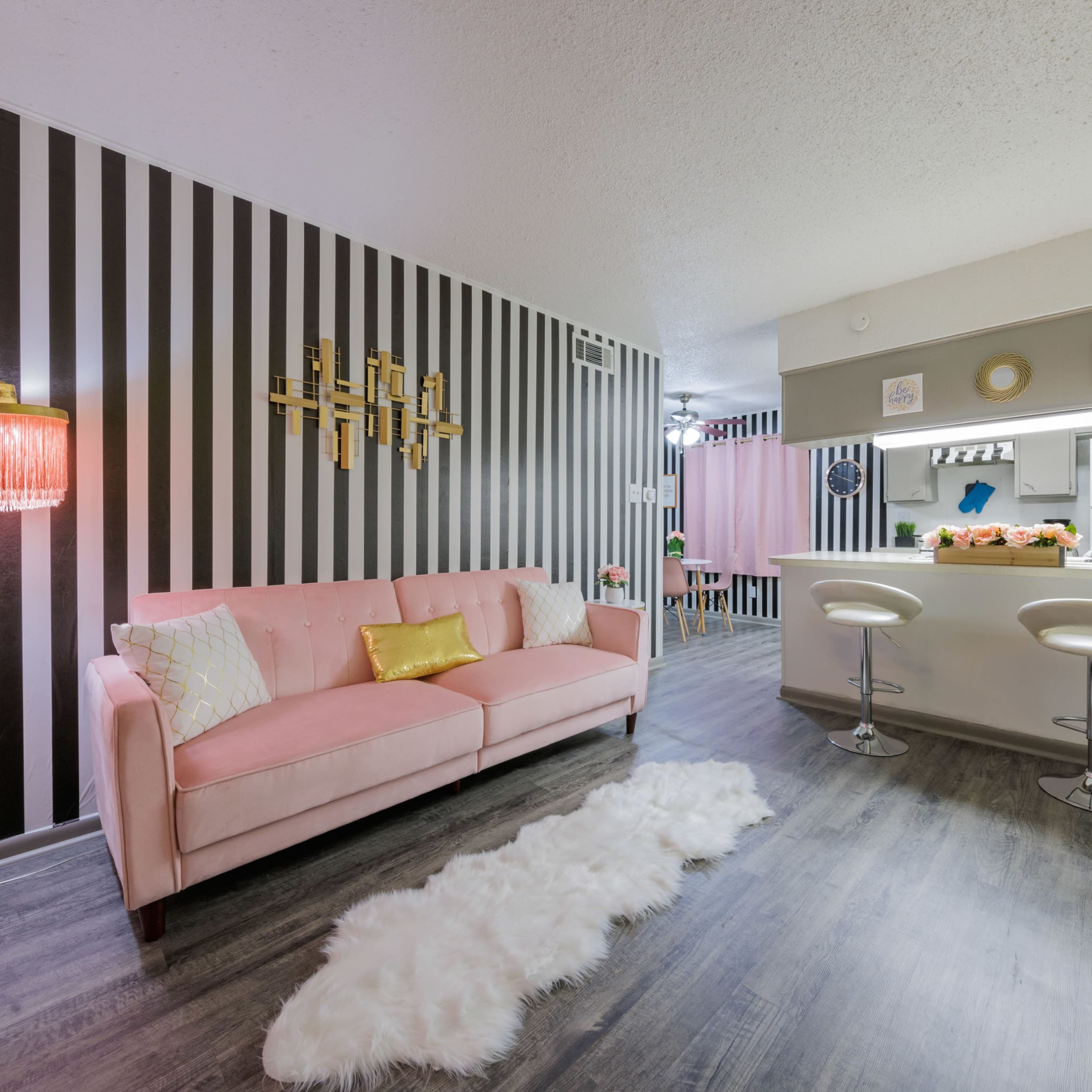 A modern living space featuring a pink sofa, a white bar area with stools, and striped wallpaper.