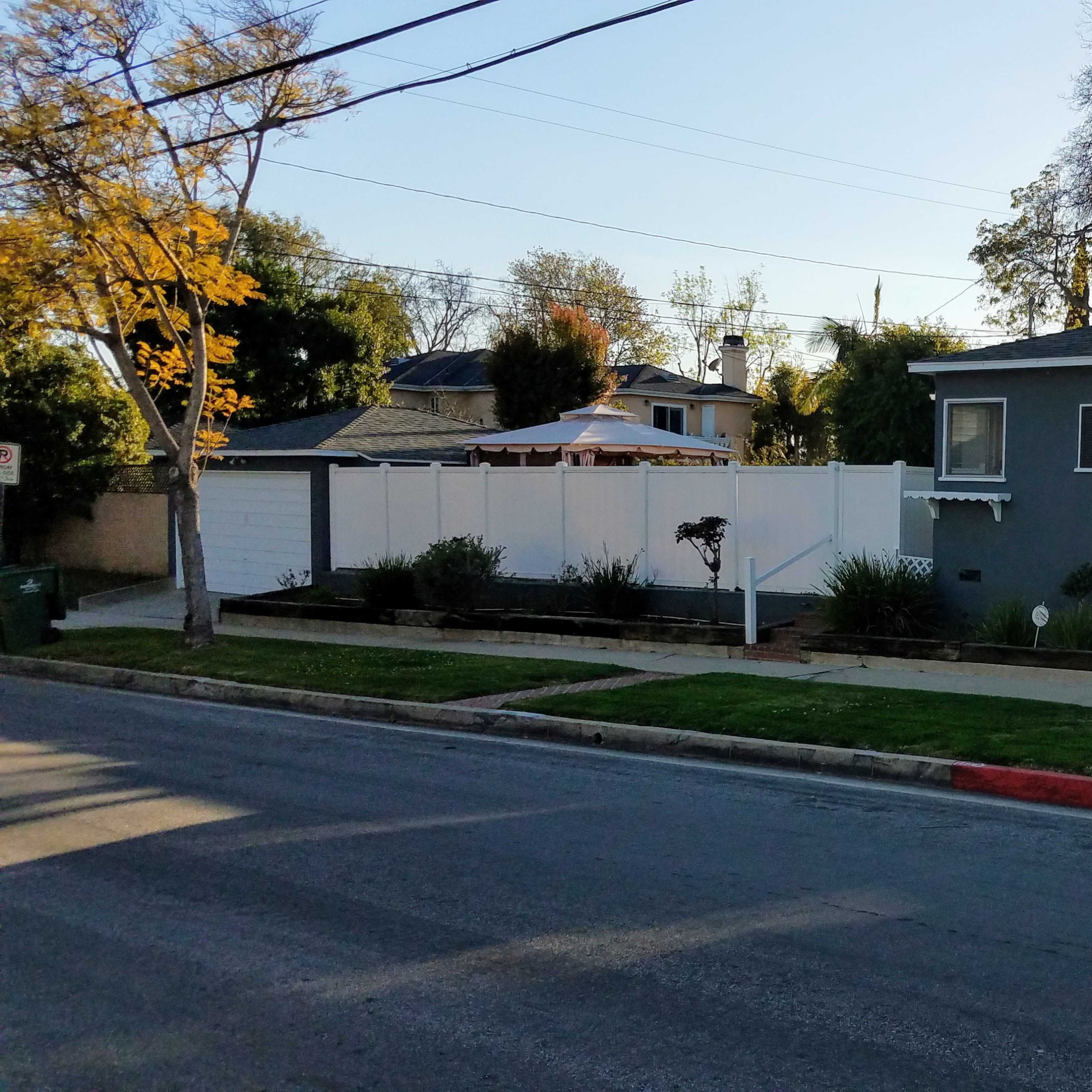 A single-story gray house with a front yard and a white fence beside a quiet street.