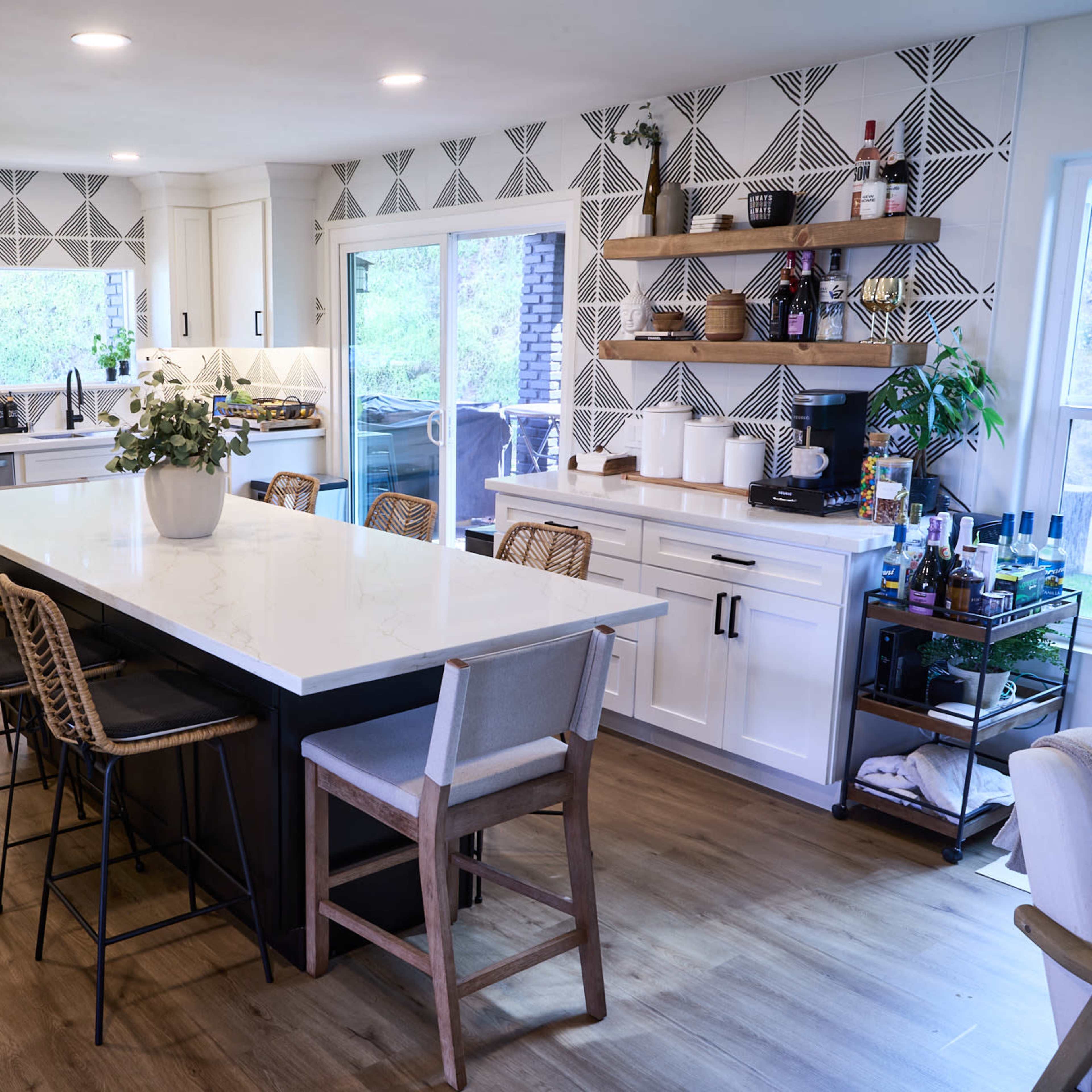 A modern kitchen with white cabinets, a large island with bar seating, and patterned wall decor.