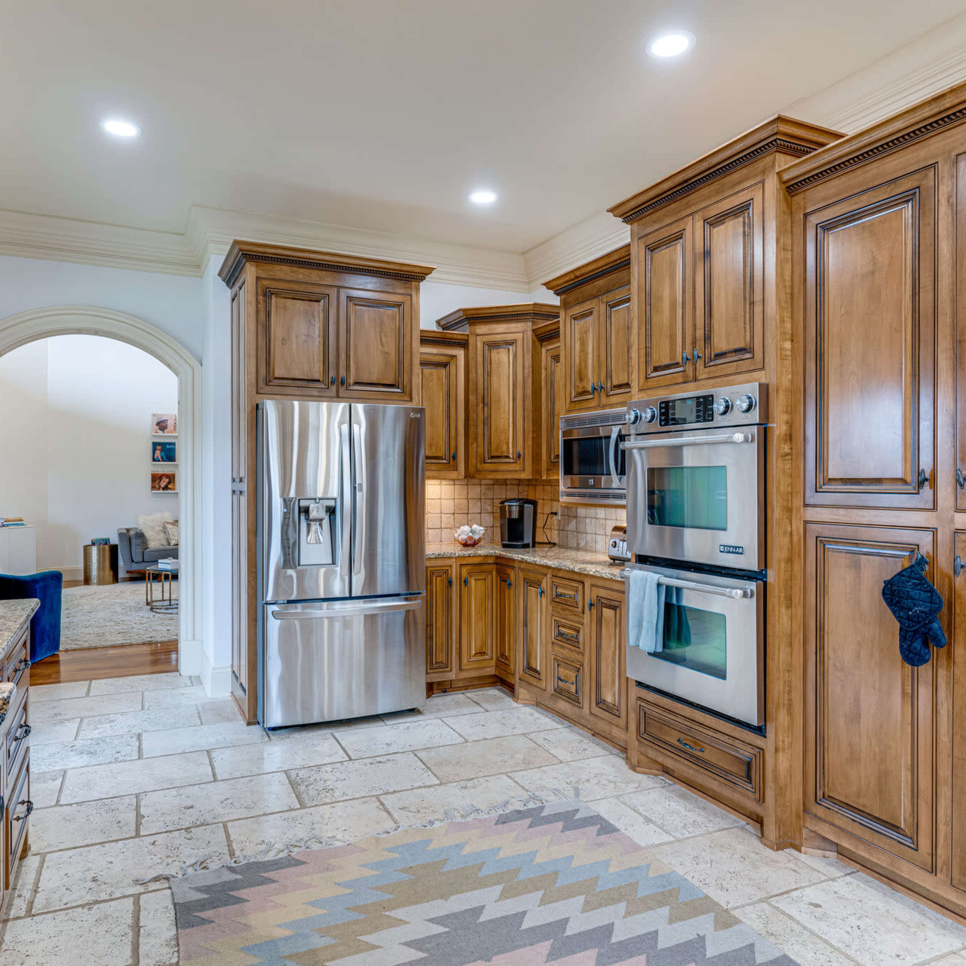 The kitchen features wooden cabinetry, stainless steel appliances, and a granite countertop, with tile flooring and a patterned rug.