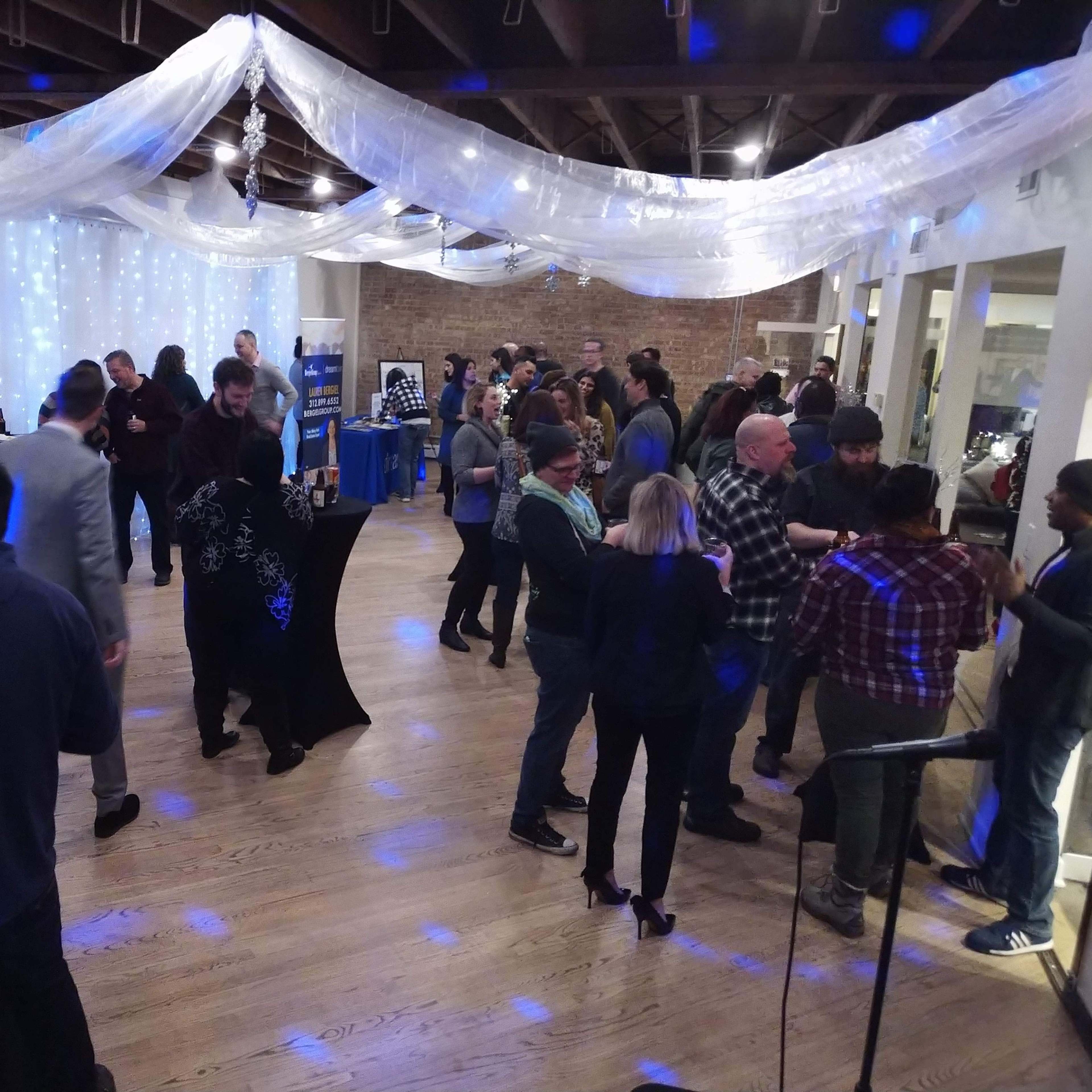 A crowded event space features people mingling under draped fabric and soft lighting.