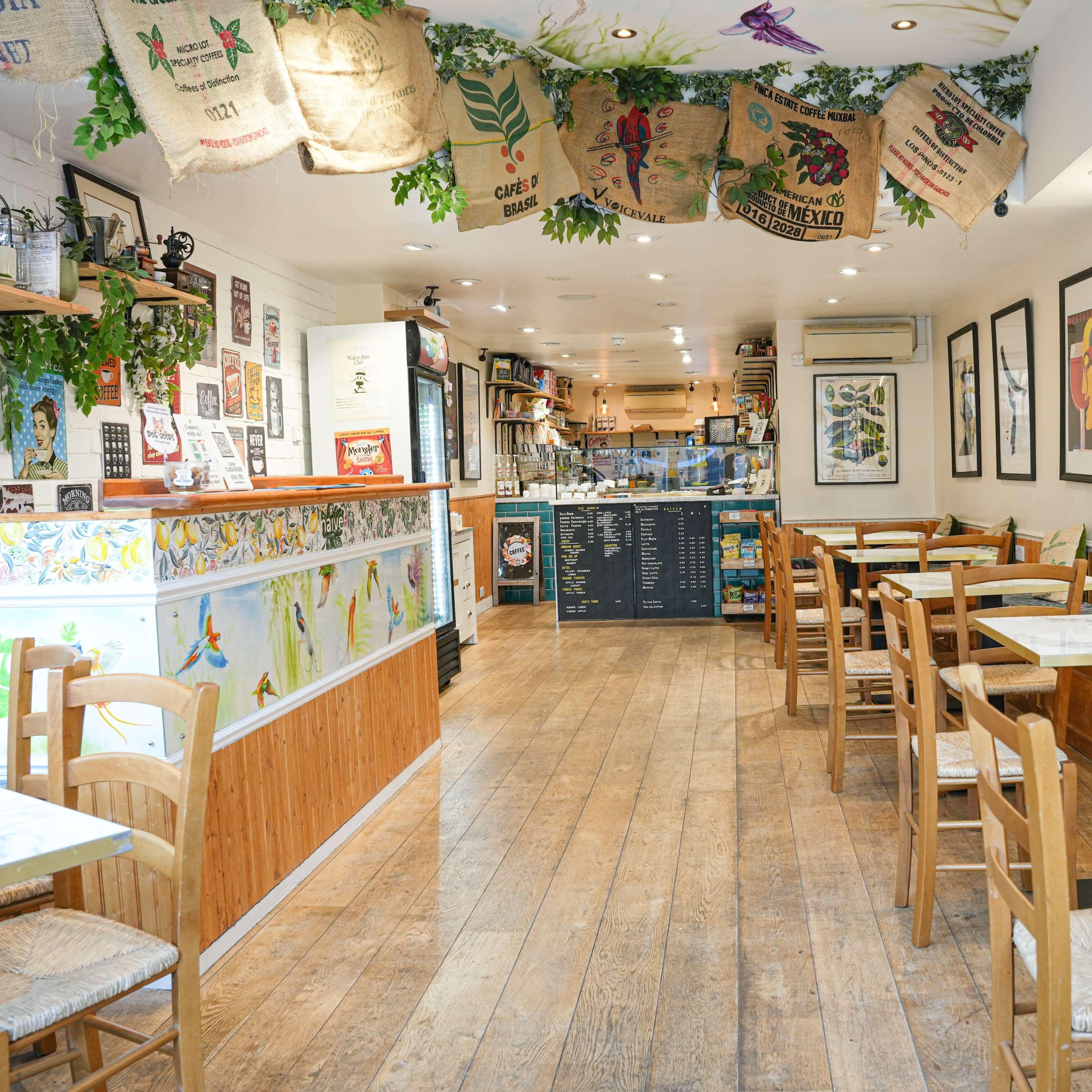 A cozy café interior with wooden tables and chairs, colorful wall art, and a counter in the background.