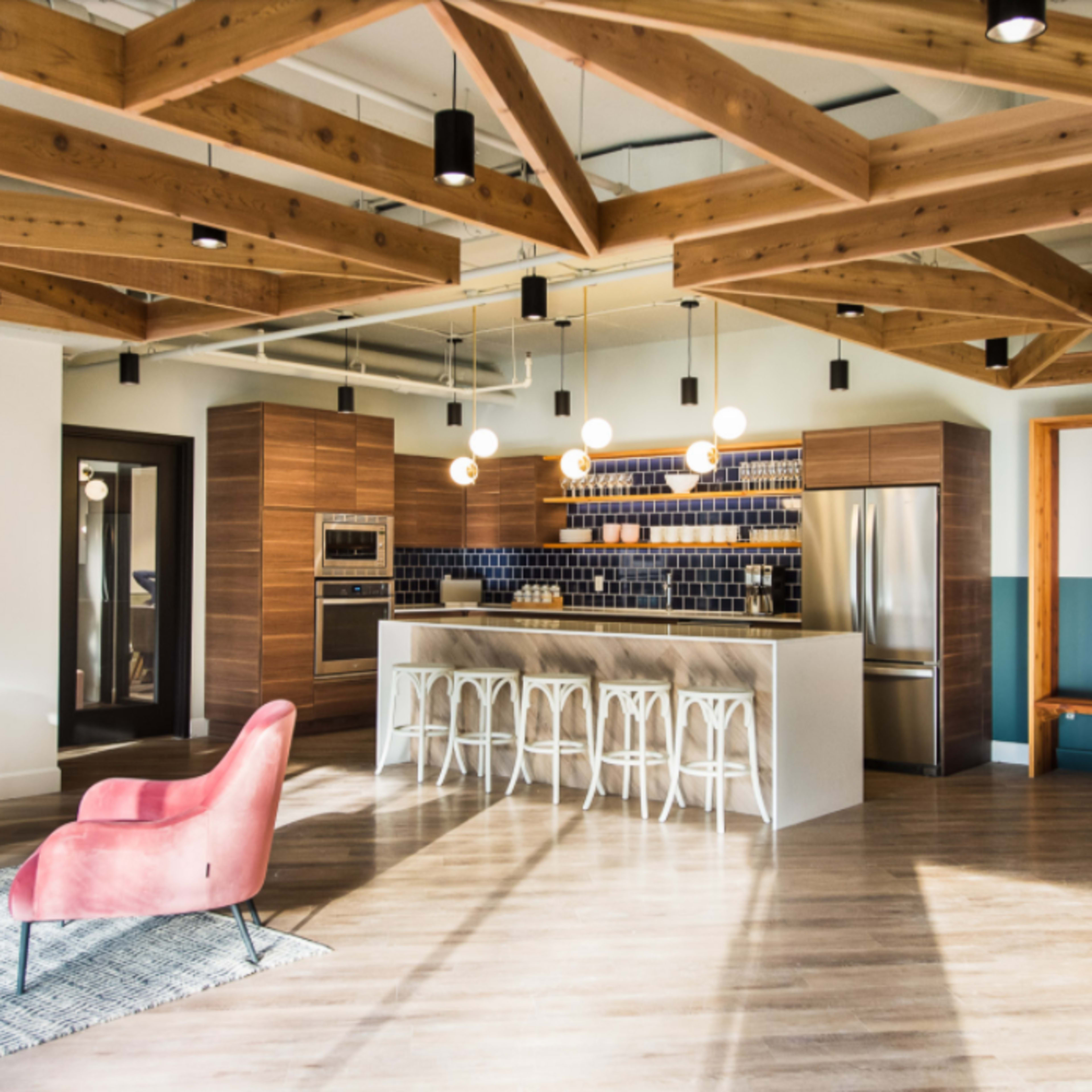 A modern kitchen with wooden beams, a central island with bar stools, and stainless steel appliances.