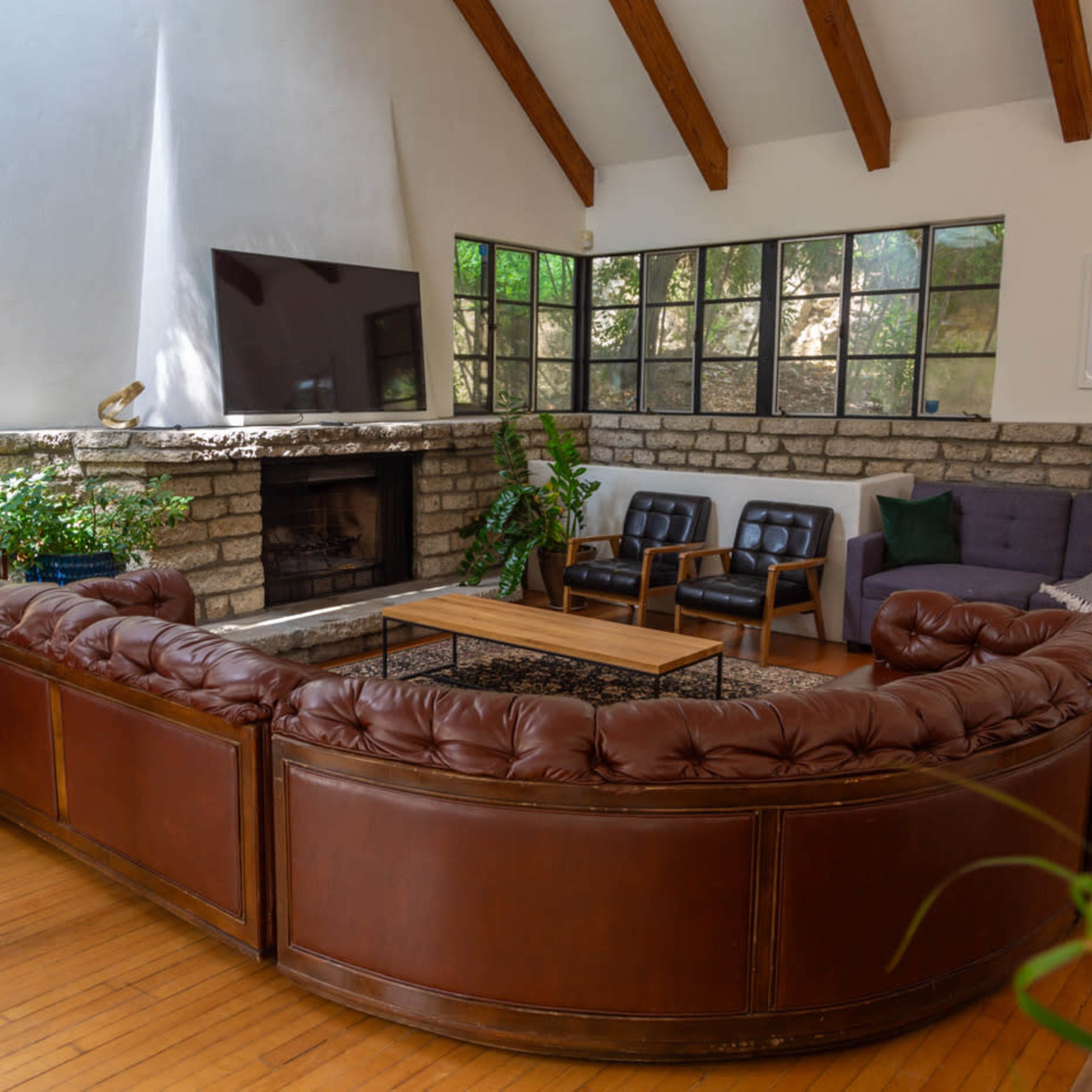 The living room features a curved leather sofa, a stone fireplace, and large windows that allow natural light to enter.