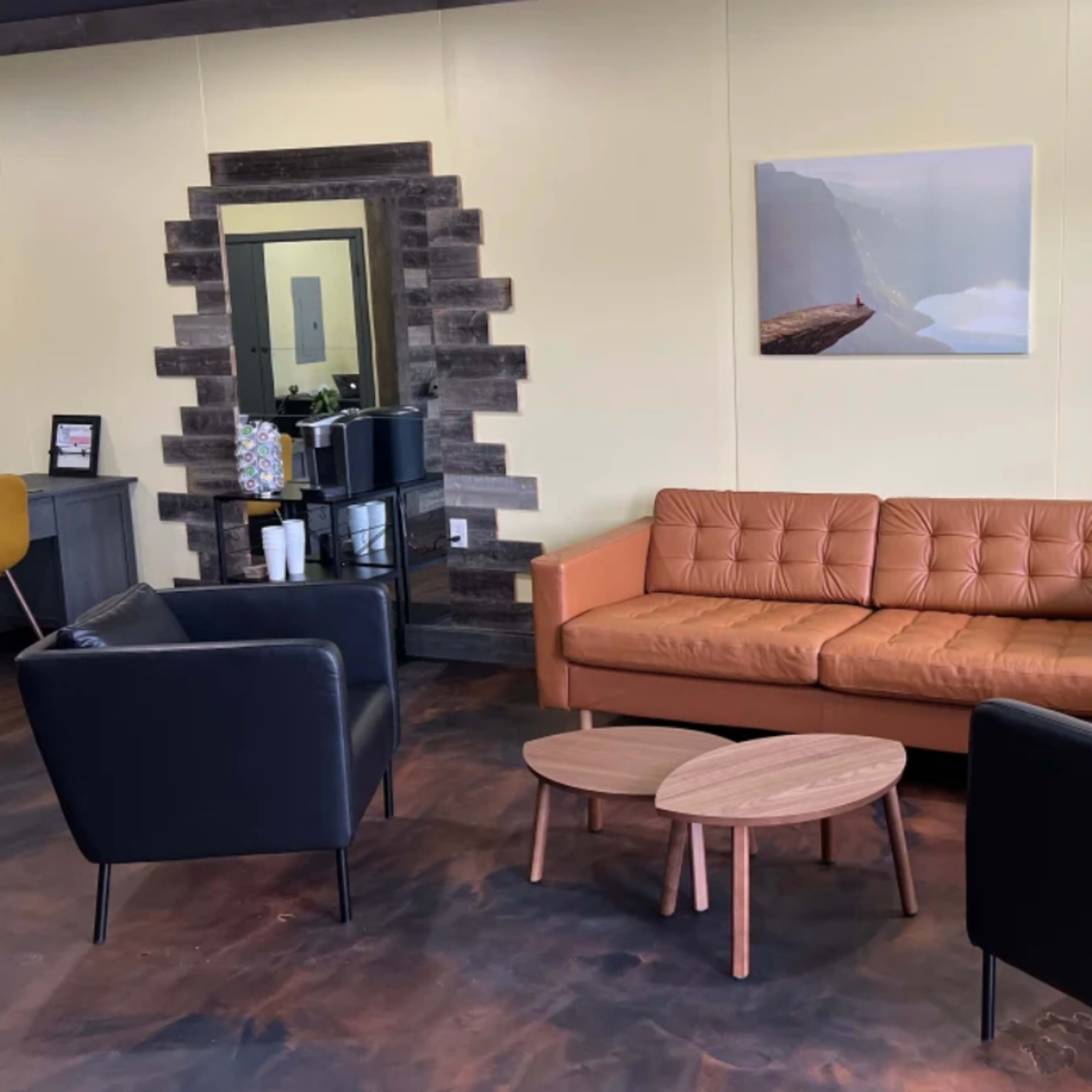 A modern seating area with a brown leather sofa, two black armchairs, and two wooden coffee tables against a yellow wall.