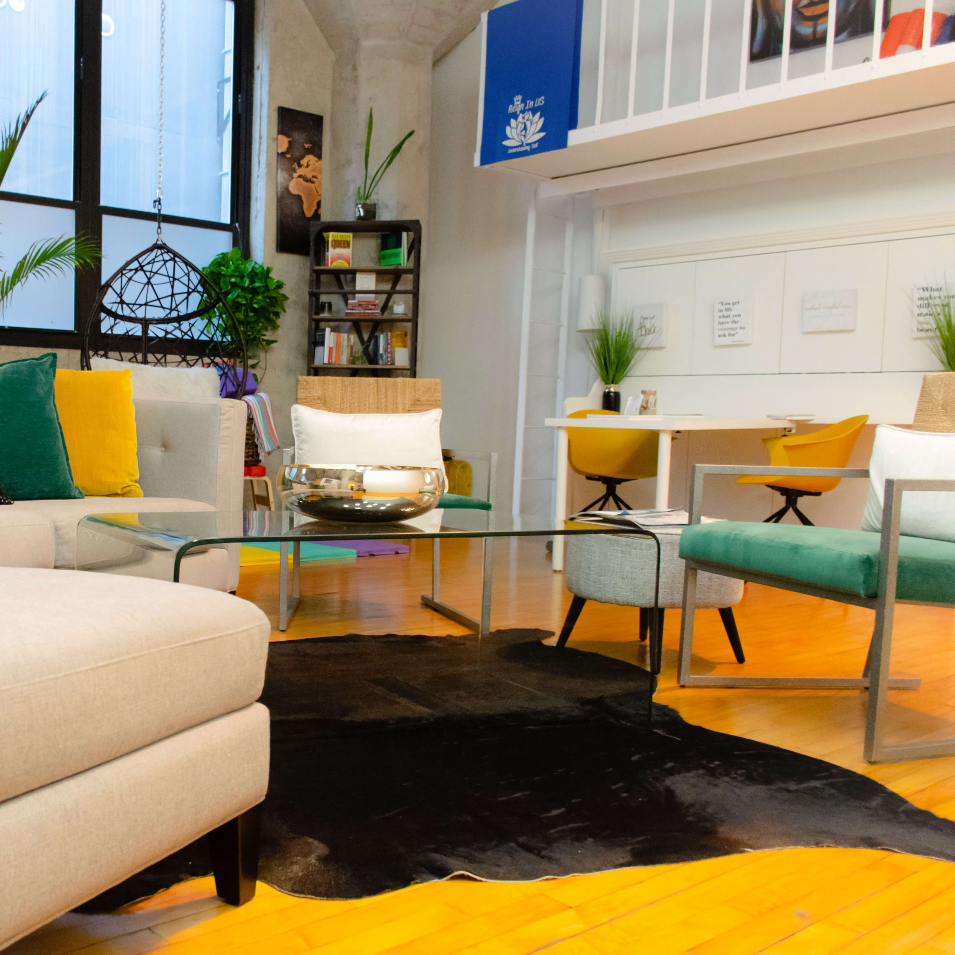 A modern living room features a sectional sofa, a glass coffee table, and various plants in bright, minimalist decor.