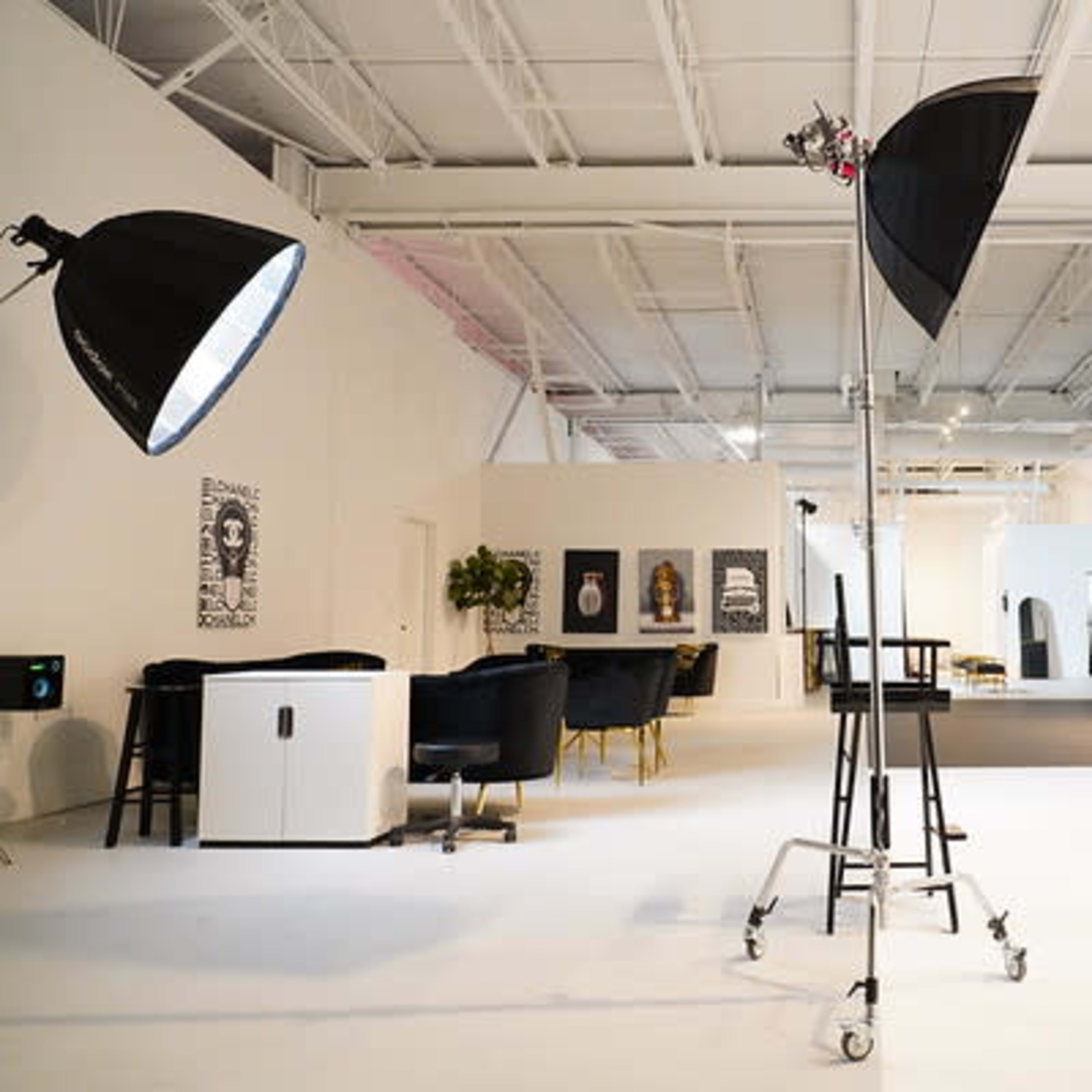 A spacious, well-lit studio features a black backdrop, photography equipment, and modern furnishings arranged around the area.