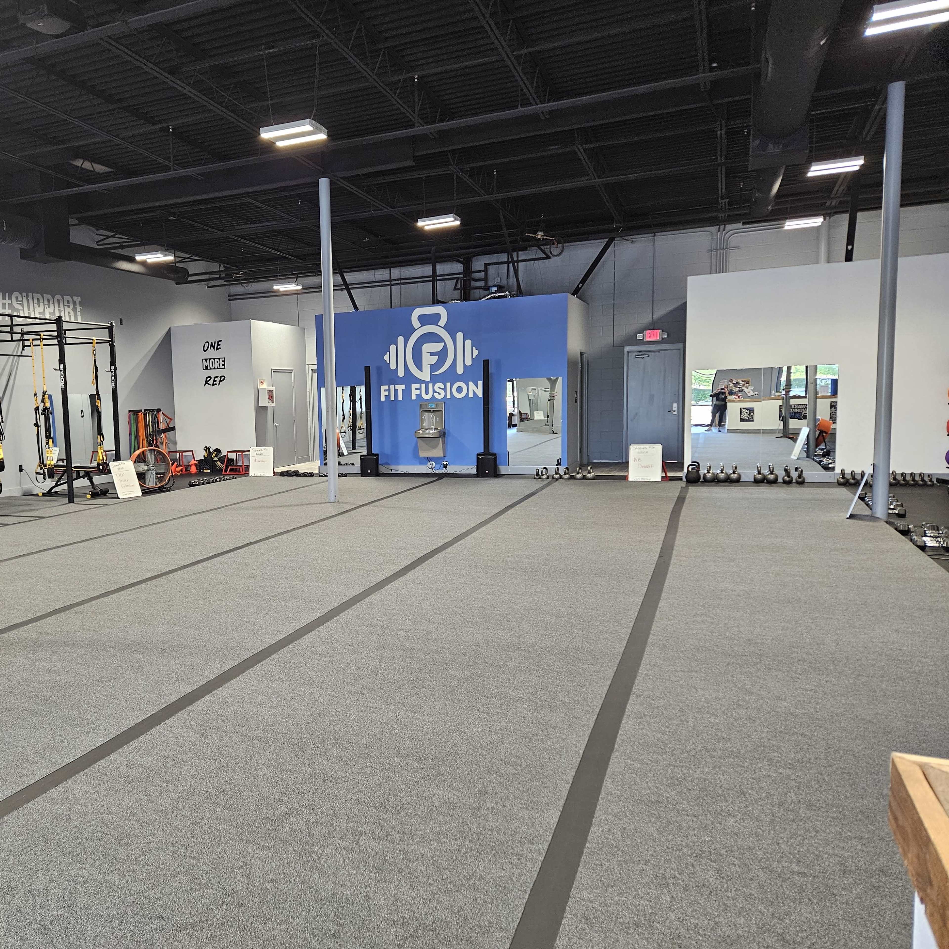 A spacious fitness studio featuring exercise equipment such as kettlebells, TRX suspension trainers, and a large blue wall with the logo "FIT FUSION."