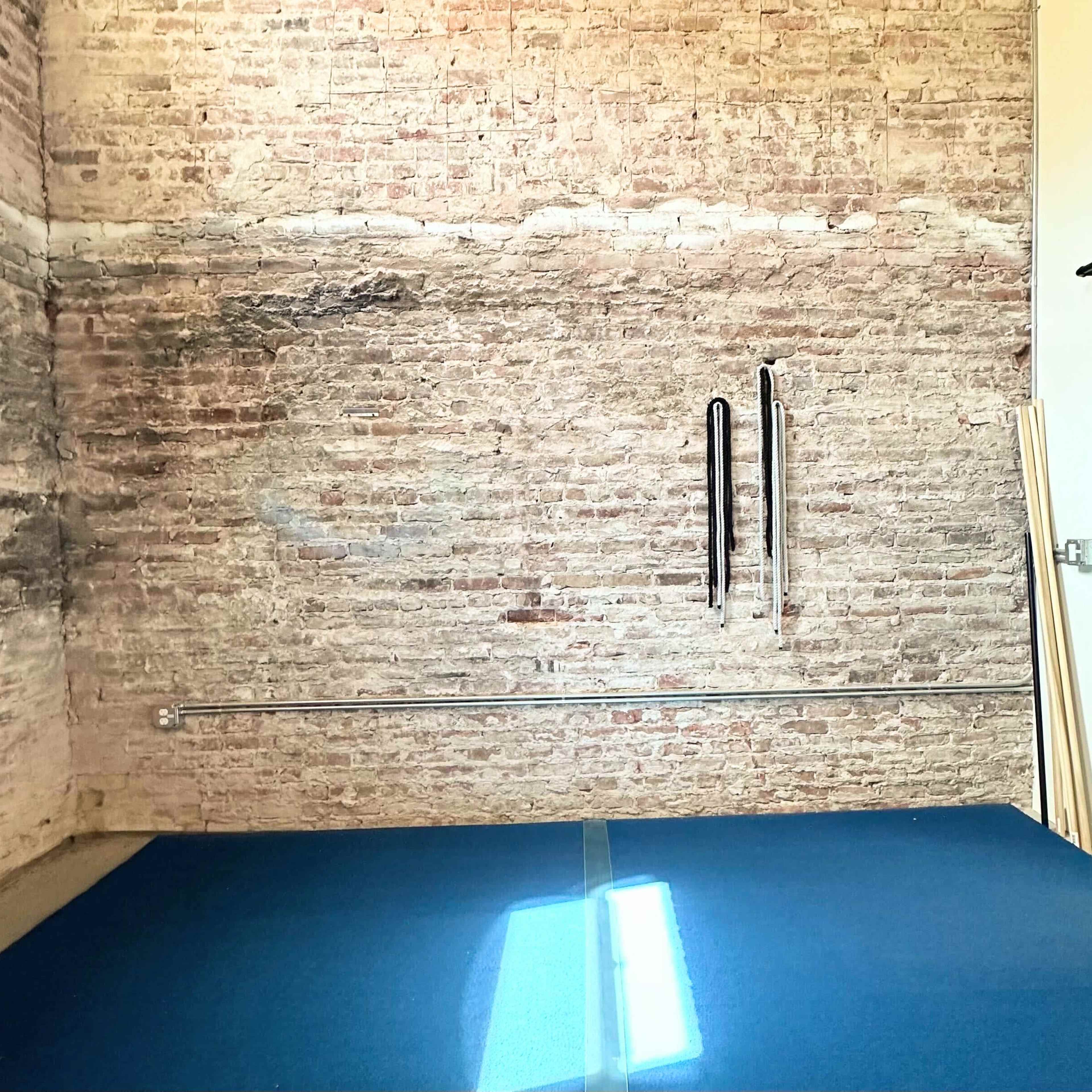 A room with a brick wall, a blue mat on the floor, and storage shelves filled with blankets and other items.