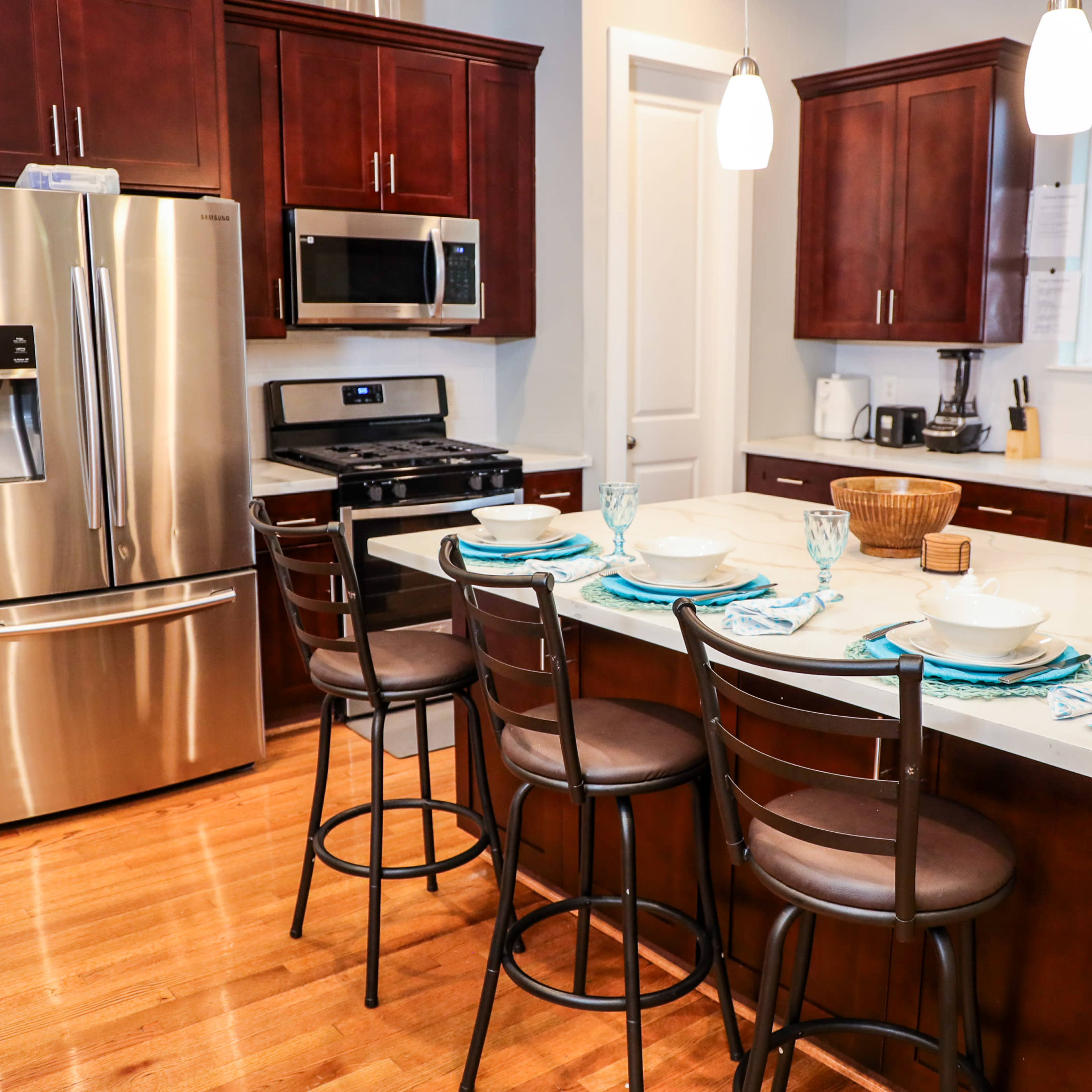 A modern kitchen features dark wood cabinetry, stainless steel appliances, and a large island with seating for four.
