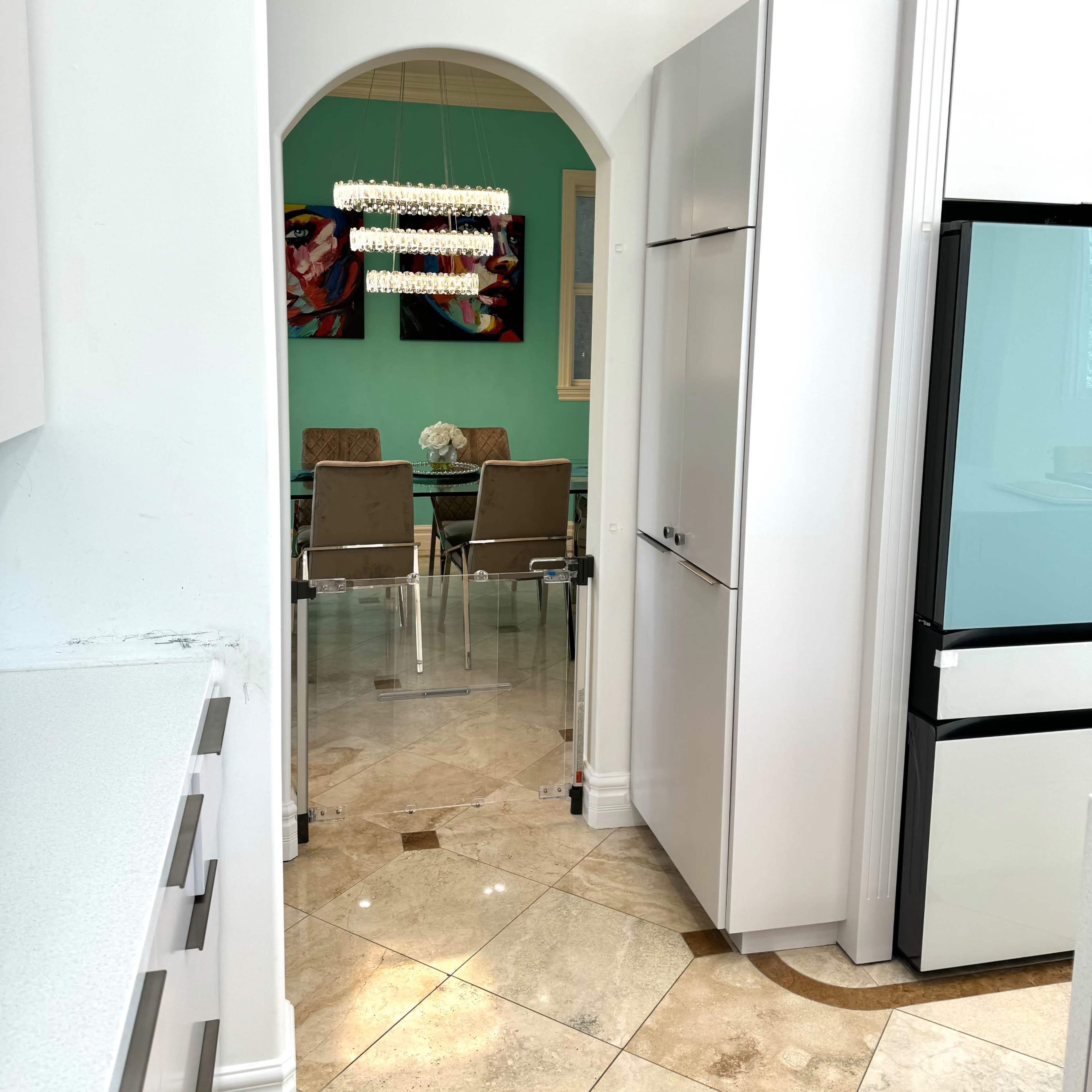 A modern kitchen with a white archway leading to a dining area featuring a turquoise wall and a glass dining table with chairs.