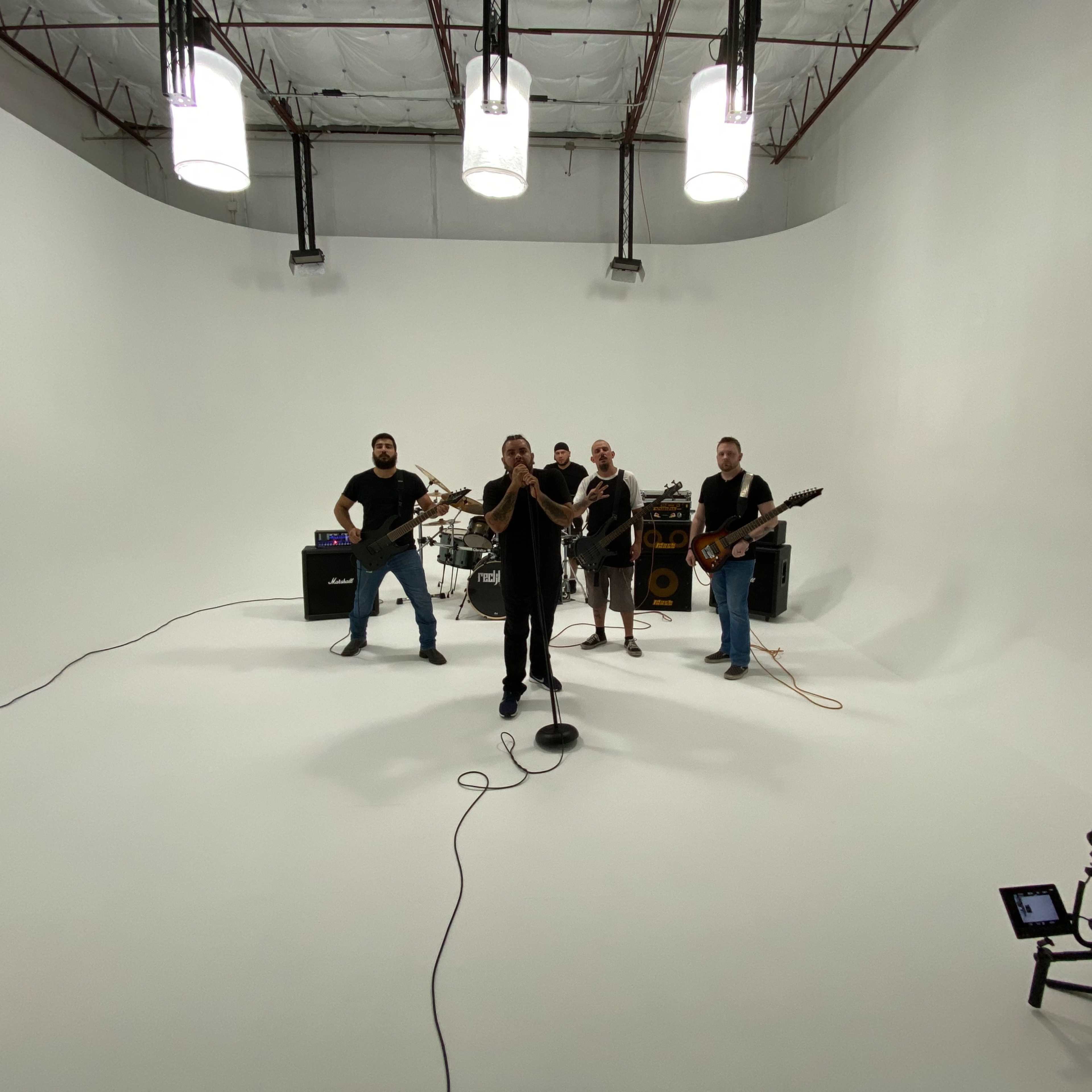 A band performs in a spacious, well-lit studio with white walls and minimal equipment.
