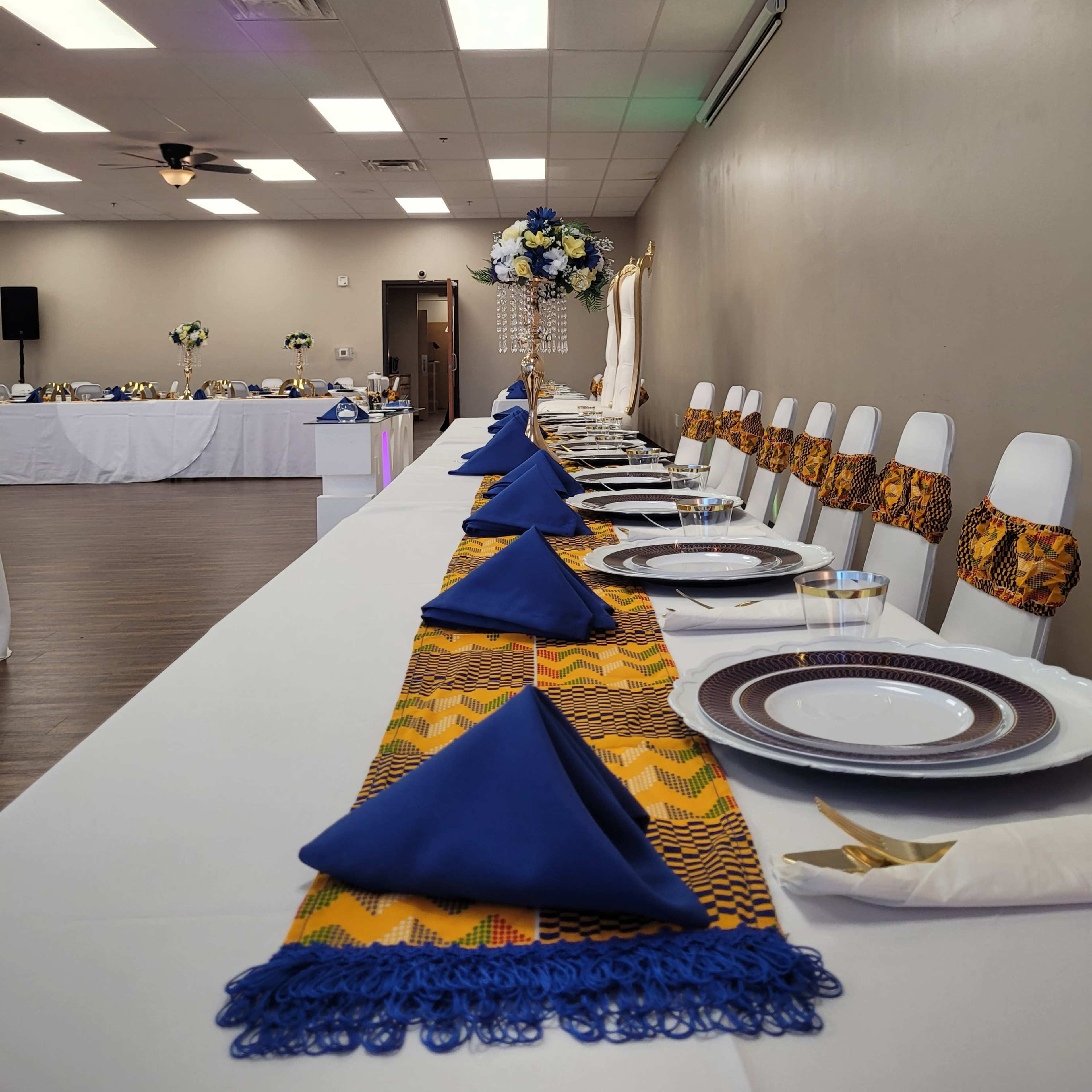 A long, elegantly set dining table is adorned with blue napkins and decorative centerpieces in a spacious event room.