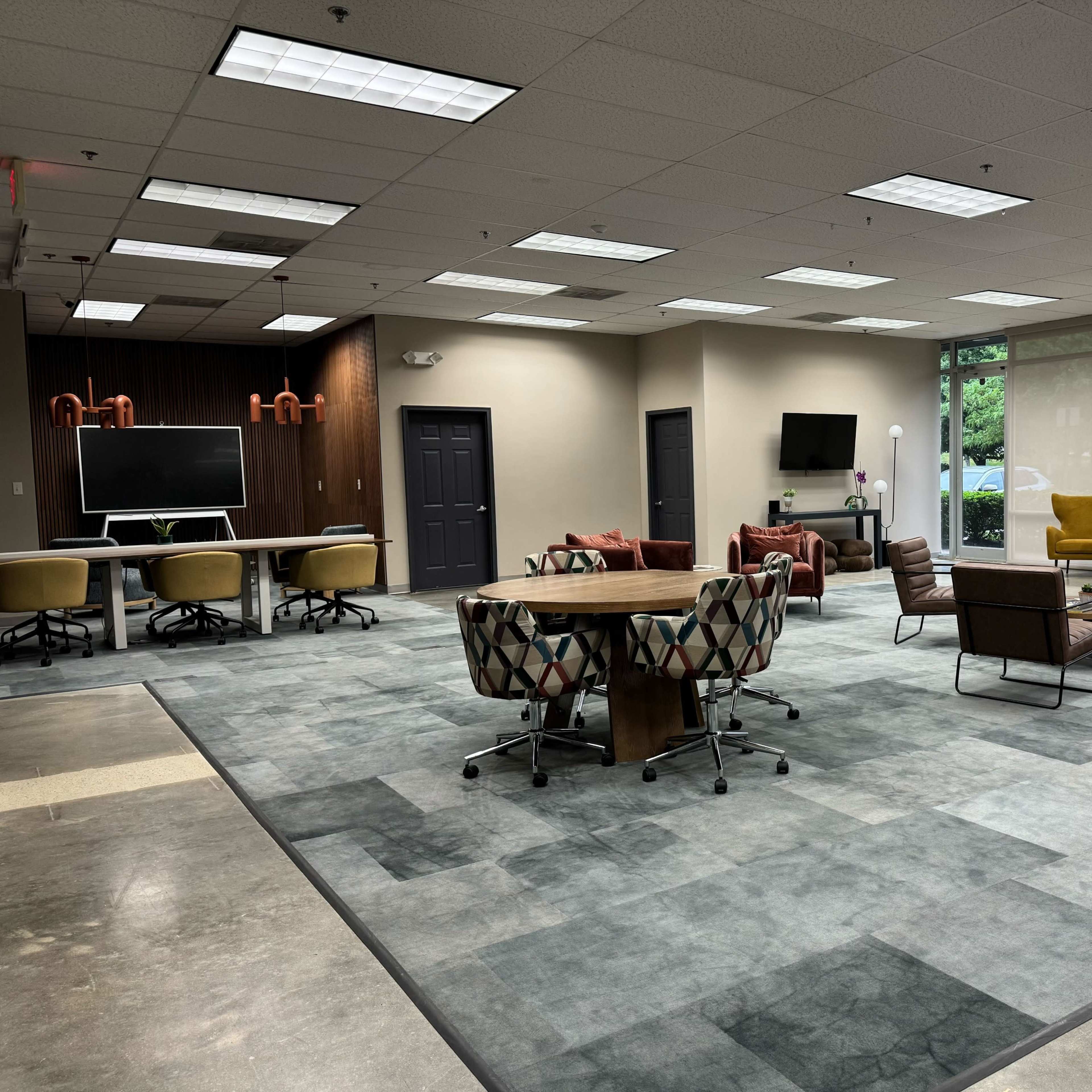 A modern office space with a large area rug, several seating arrangements, and workstations featuring monitors and chairs.