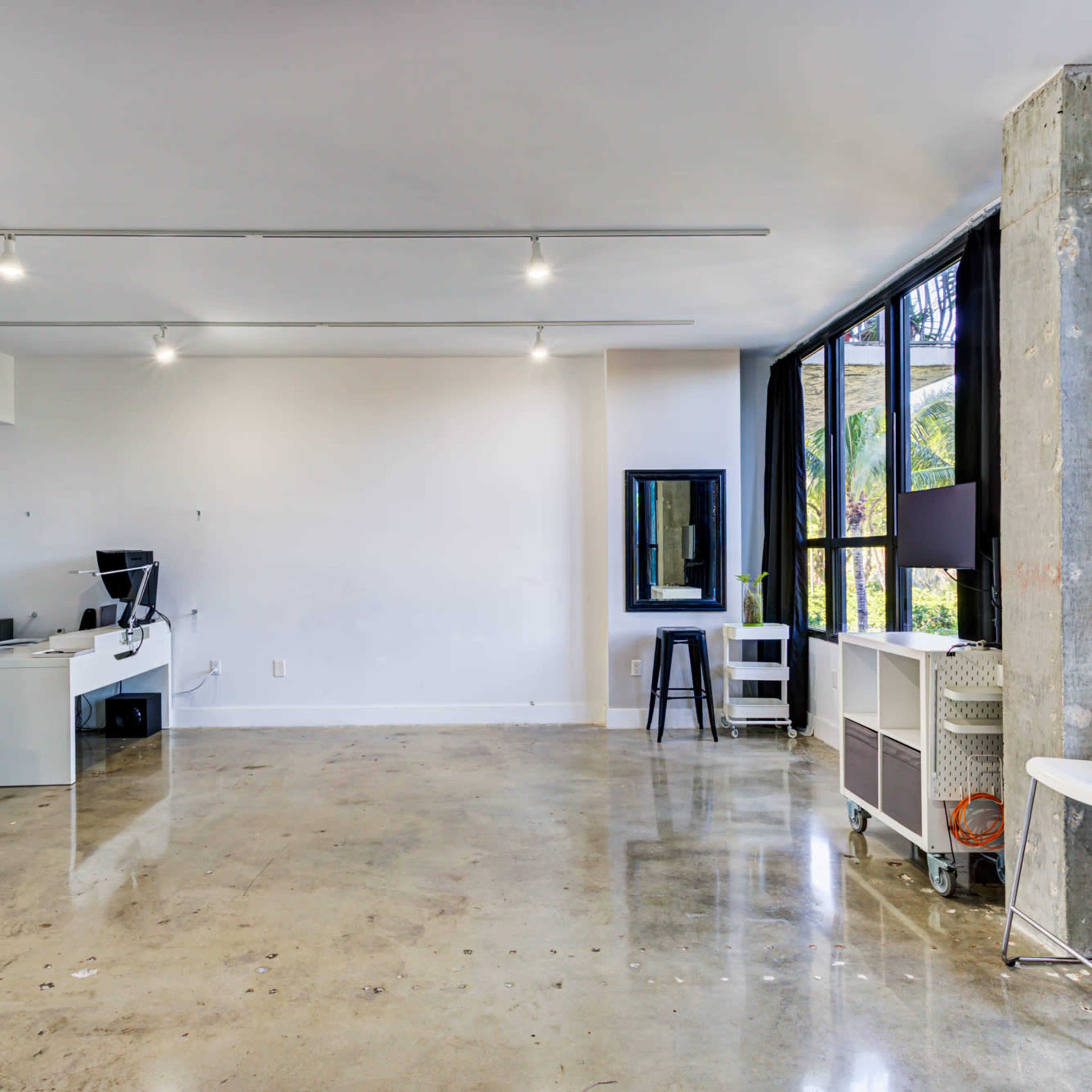 An open office space with polished concrete floors, a desk and office chair, and large windows allowing natural light.