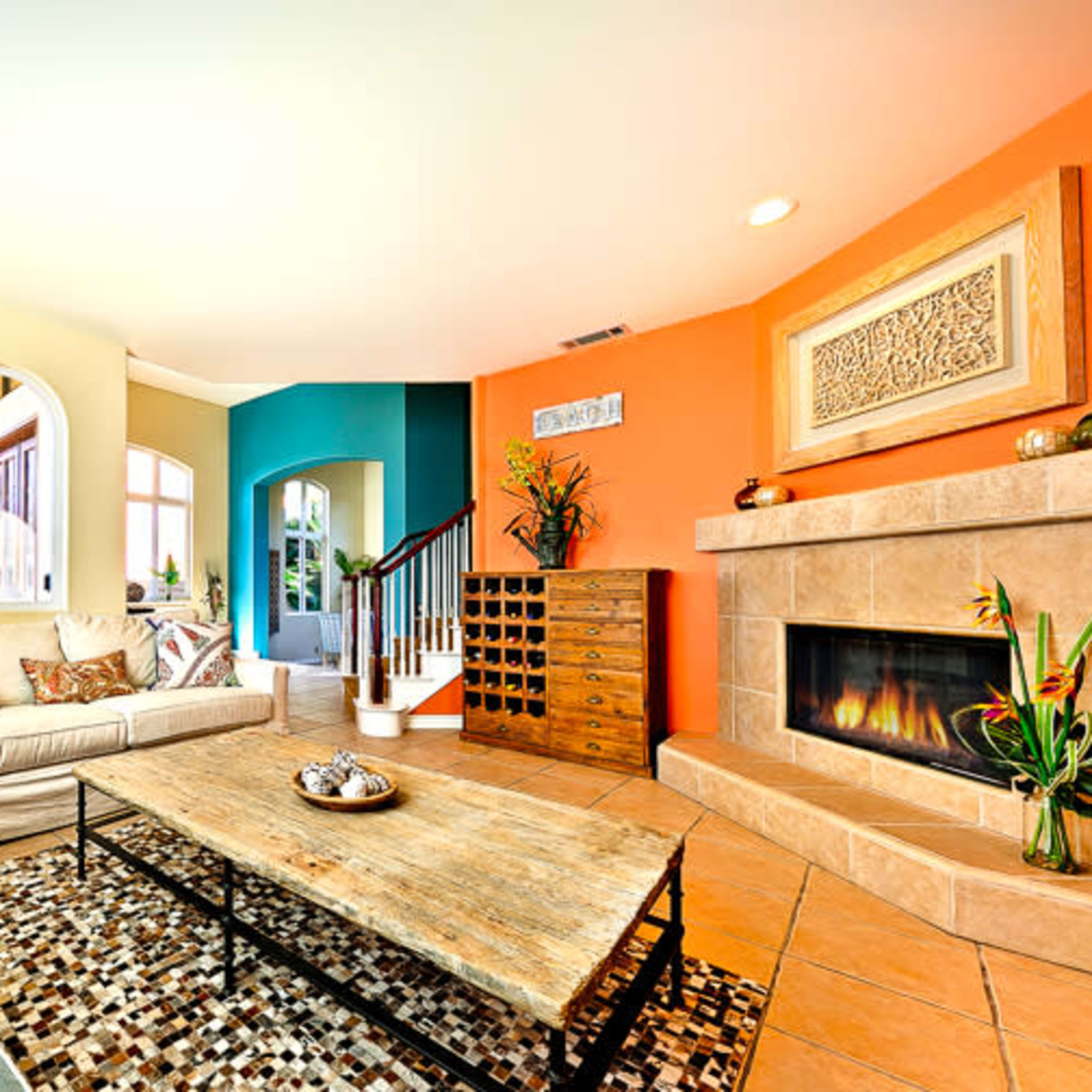 The living room features a beige sofa and a blue accent chair surrounding a wooden coffee table, with a stone fireplace and colorful walls.