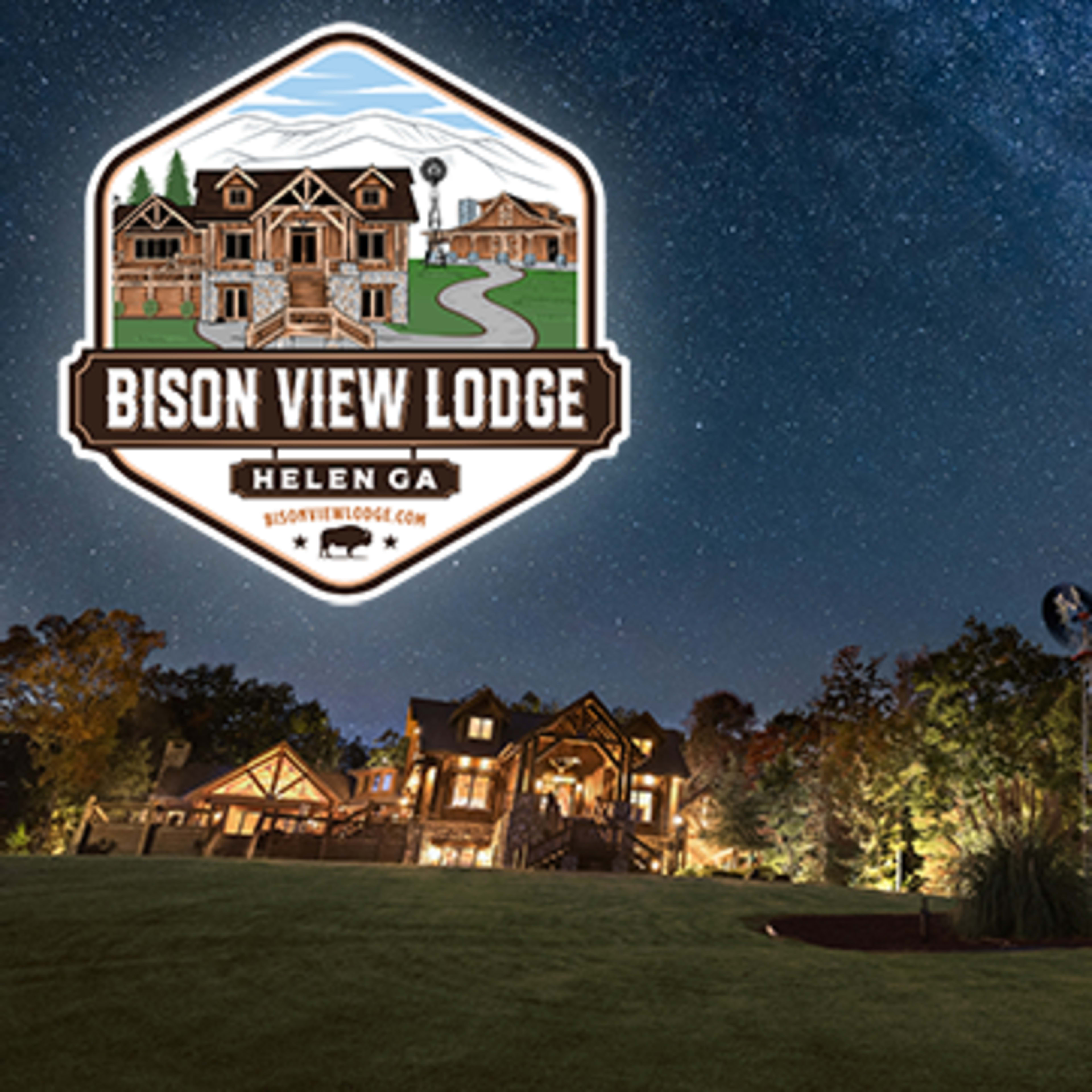 The Bison View Lodge in Helen, GA, set against a starry night sky, with a windmill and rustic equipment in the foreground.