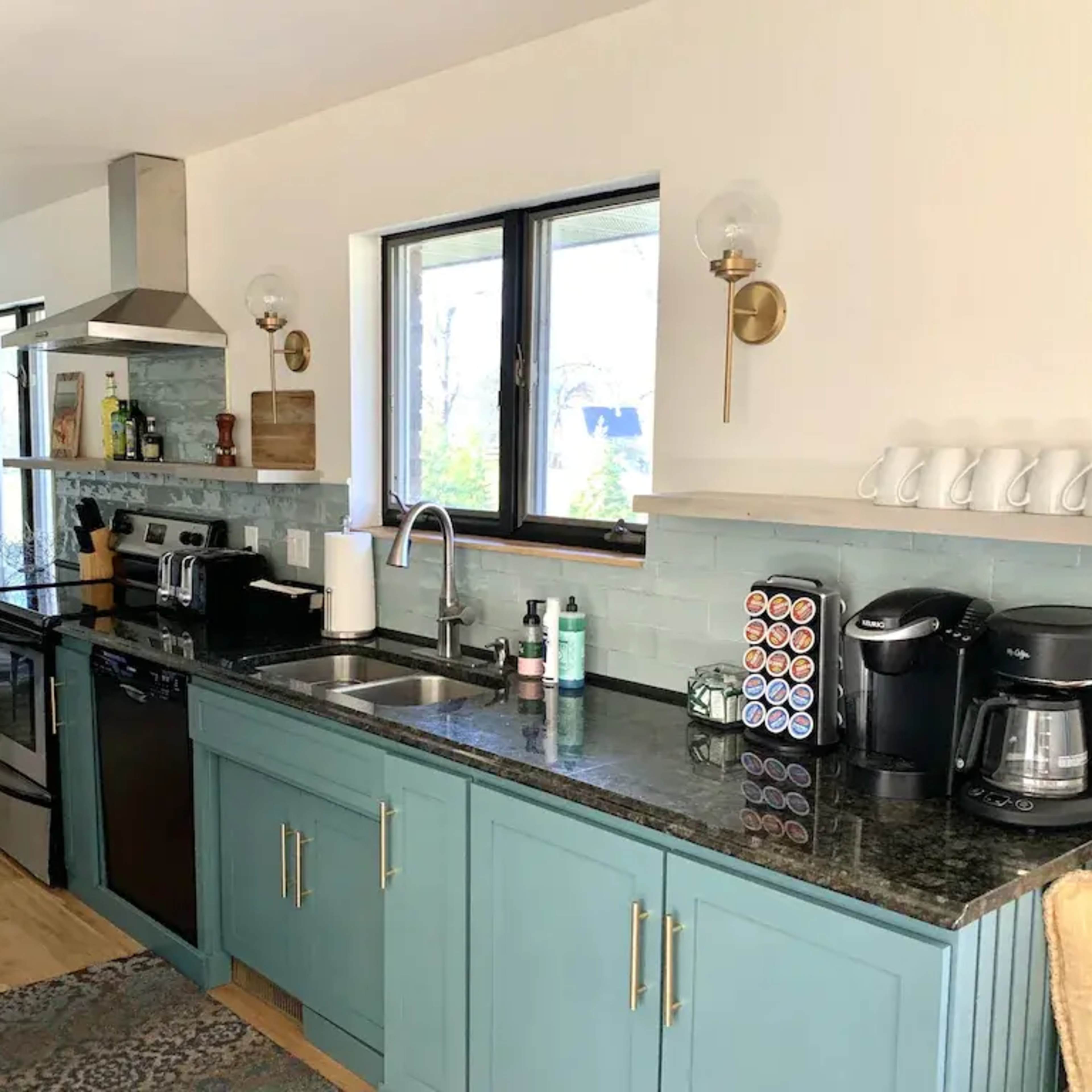 A modern kitchen with teal cabinetry, a stainless steel stove and microwave, and an organized countertop featuring various kitchen appliances.