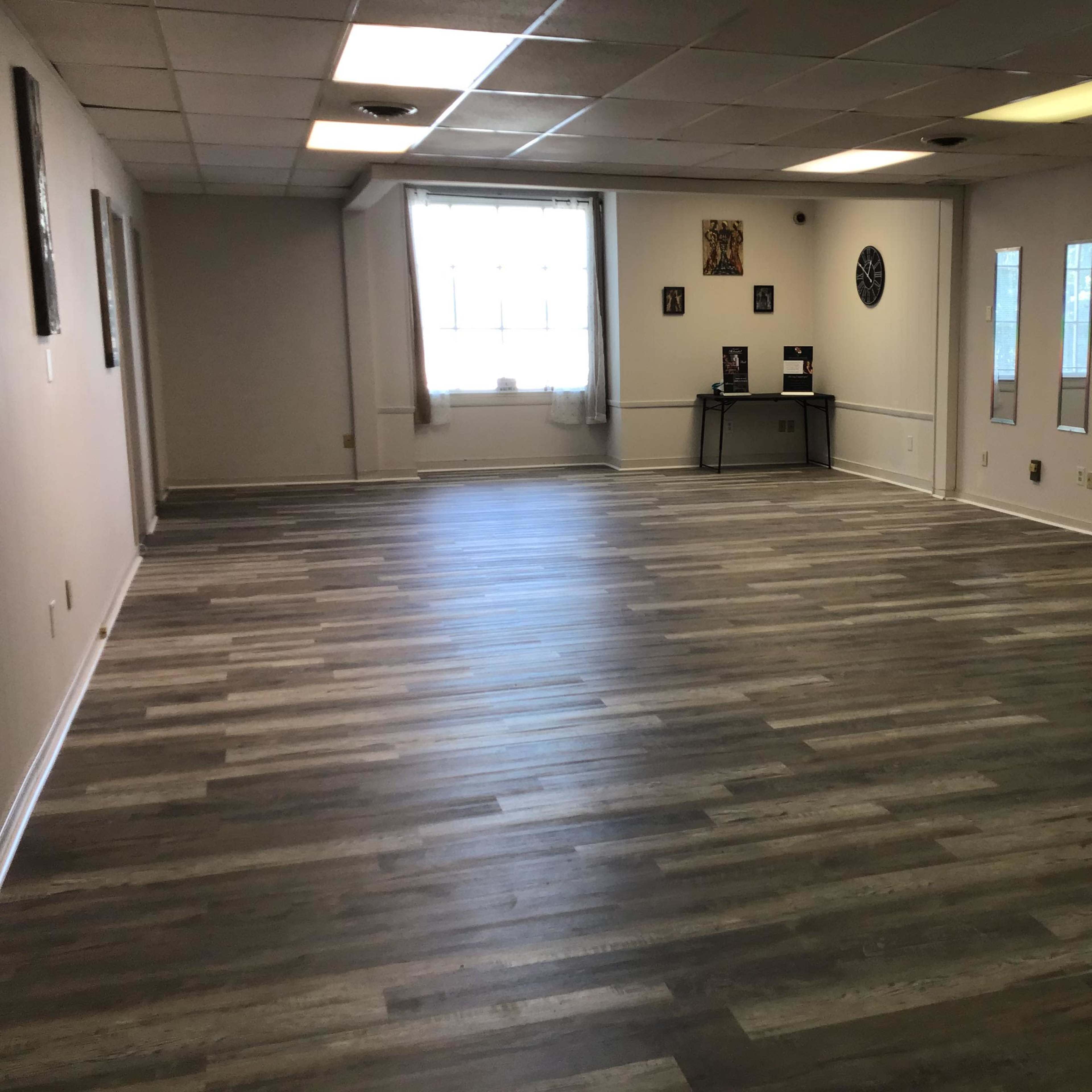 A spacious, empty room with a hardwood floor and windows allowing natural light.