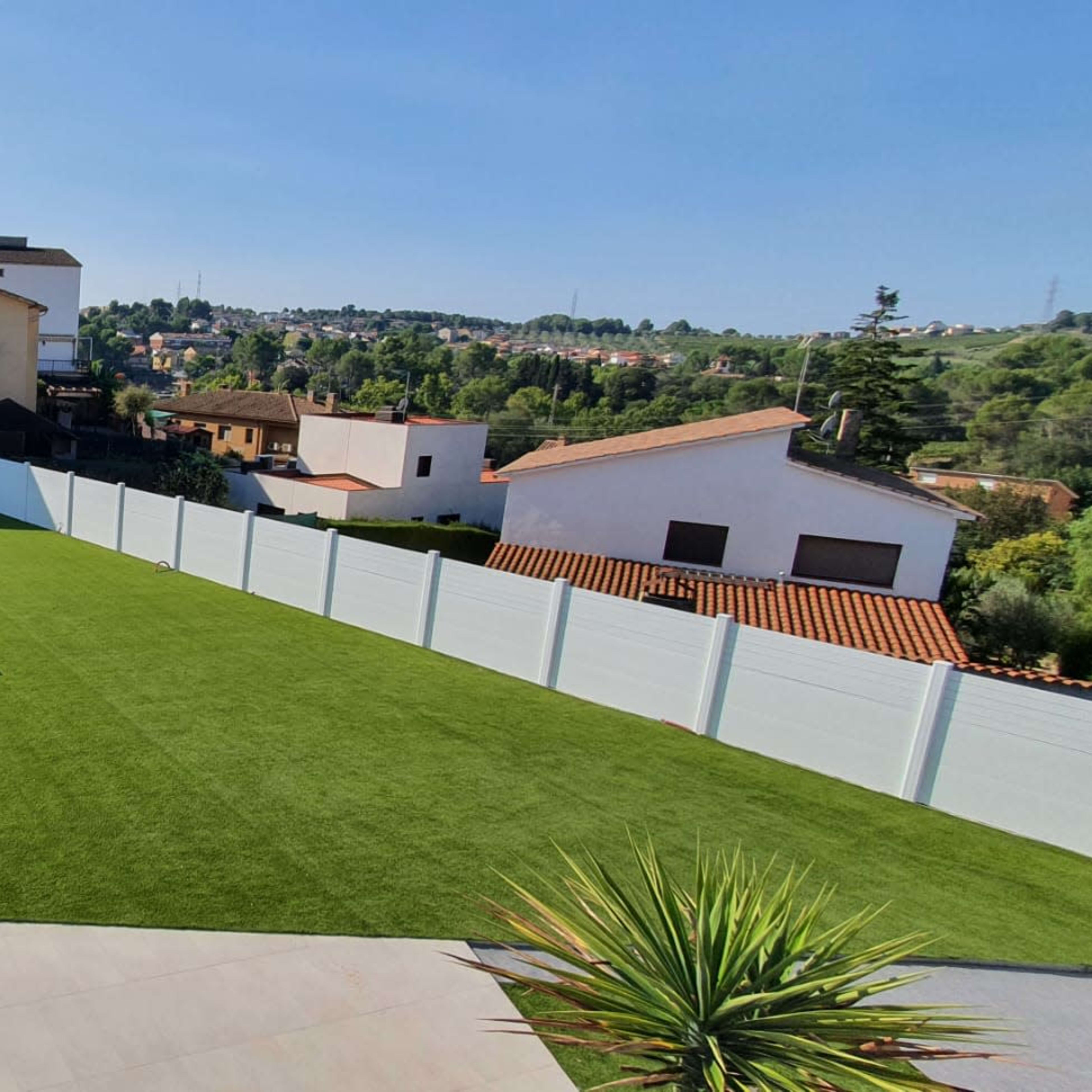 A backyard with a swimming pool, lounge chairs, and a well-maintained lawn, surrounded by white fences and residential buildings in the background.