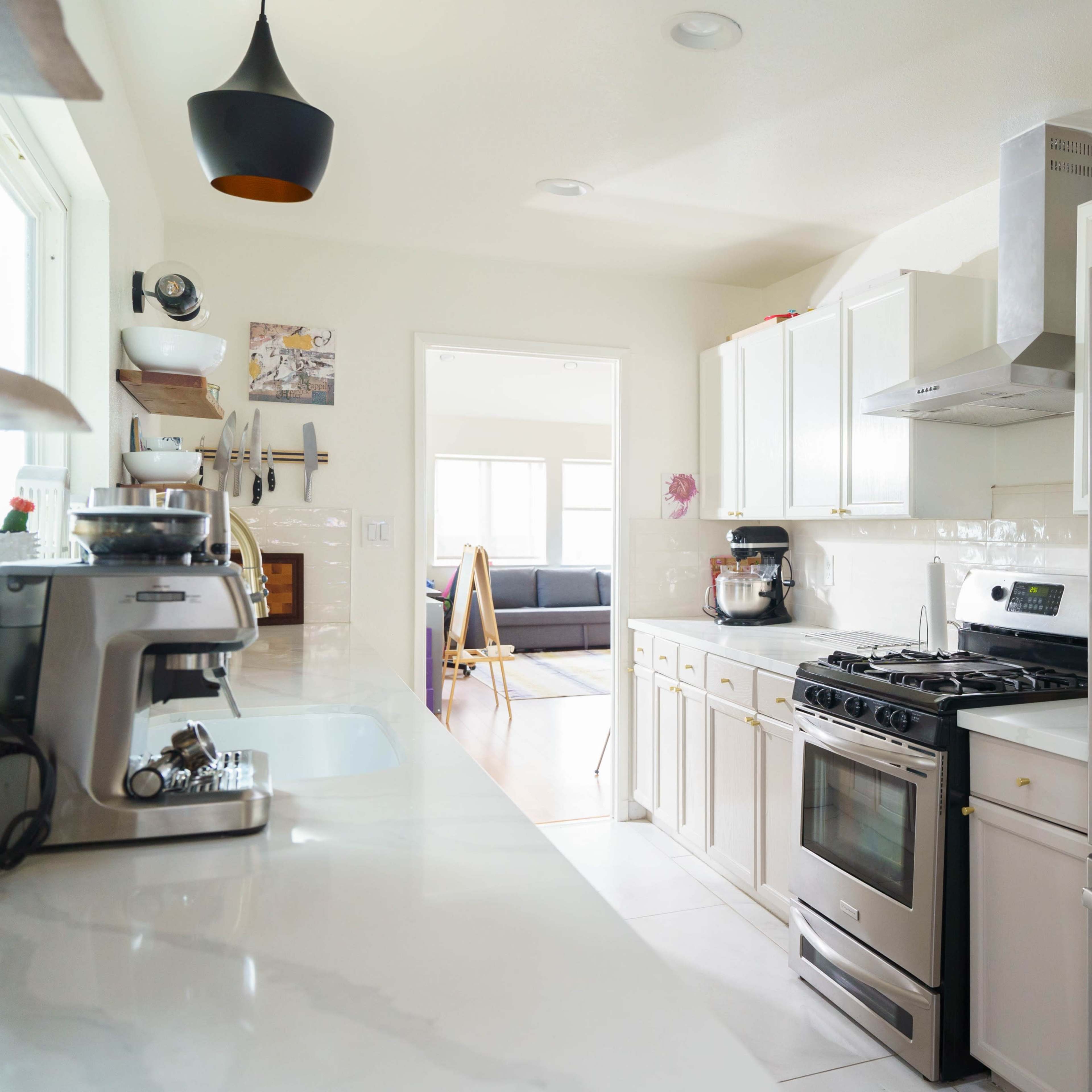 A modern kitchen with stainless steel appliances, including a refrigerator and a gas range, along with white cabinetry and a marble countertop.