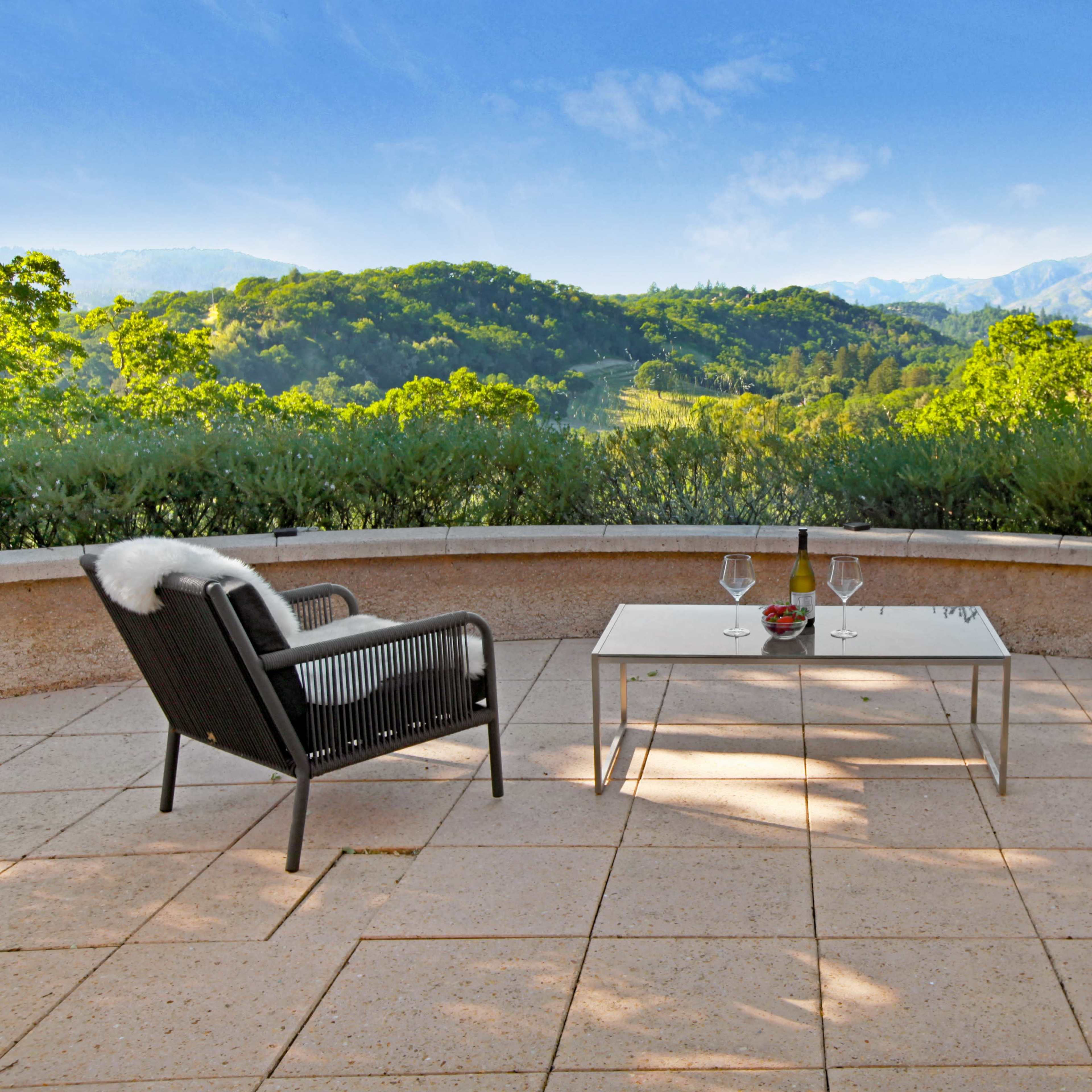A patio features two chairs and a table with a view of rolling hills and mountains in the background.