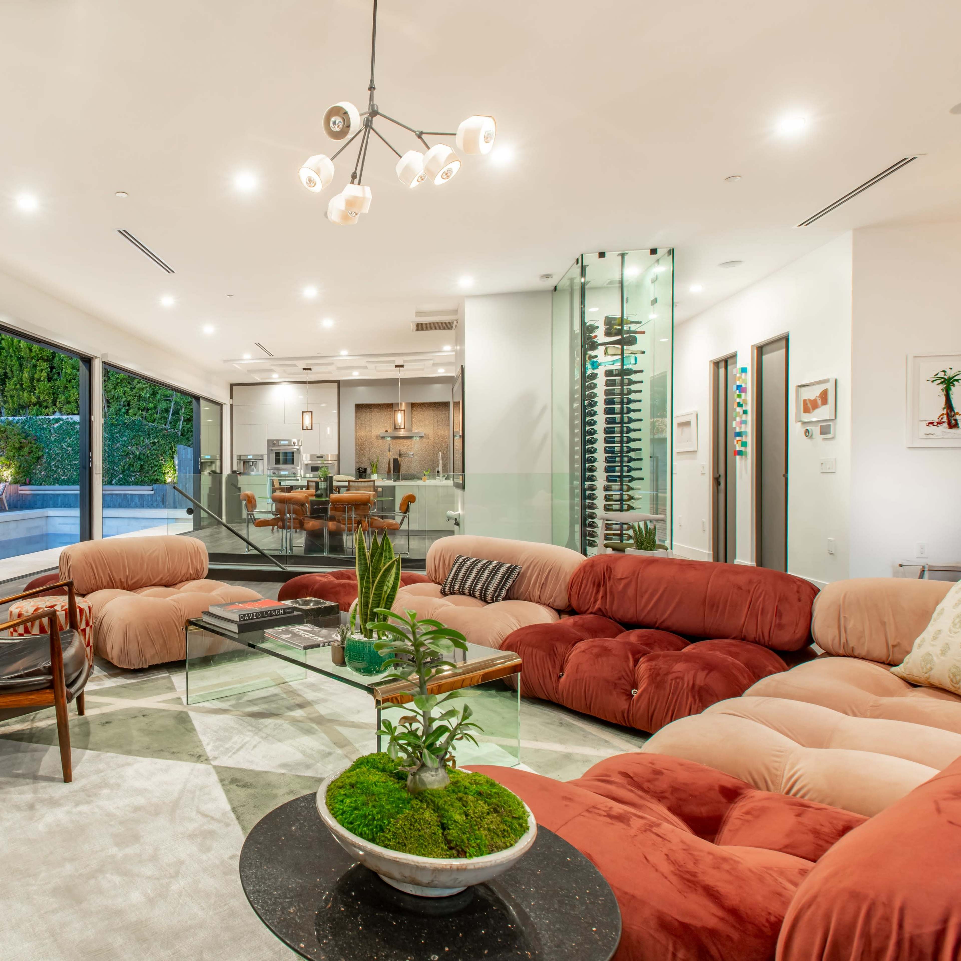 A modern living room with a large, plush sectional couch, a glass coffee table, and floor-to-ceiling windows that overlook a backyard swimming pool.
