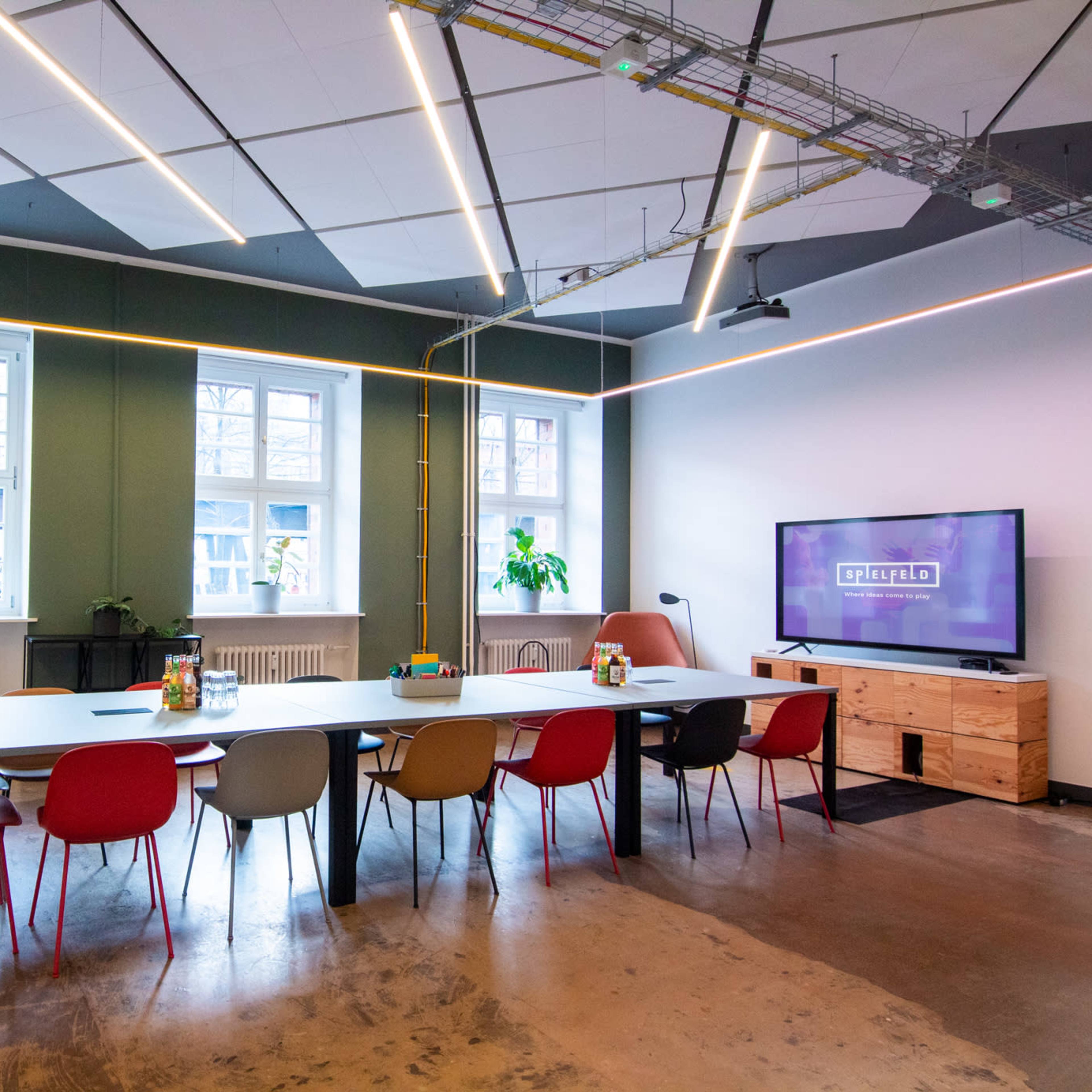 A modern conference room with a long table, colorful chairs, a whiteboard, and a TV mounted on the wall.