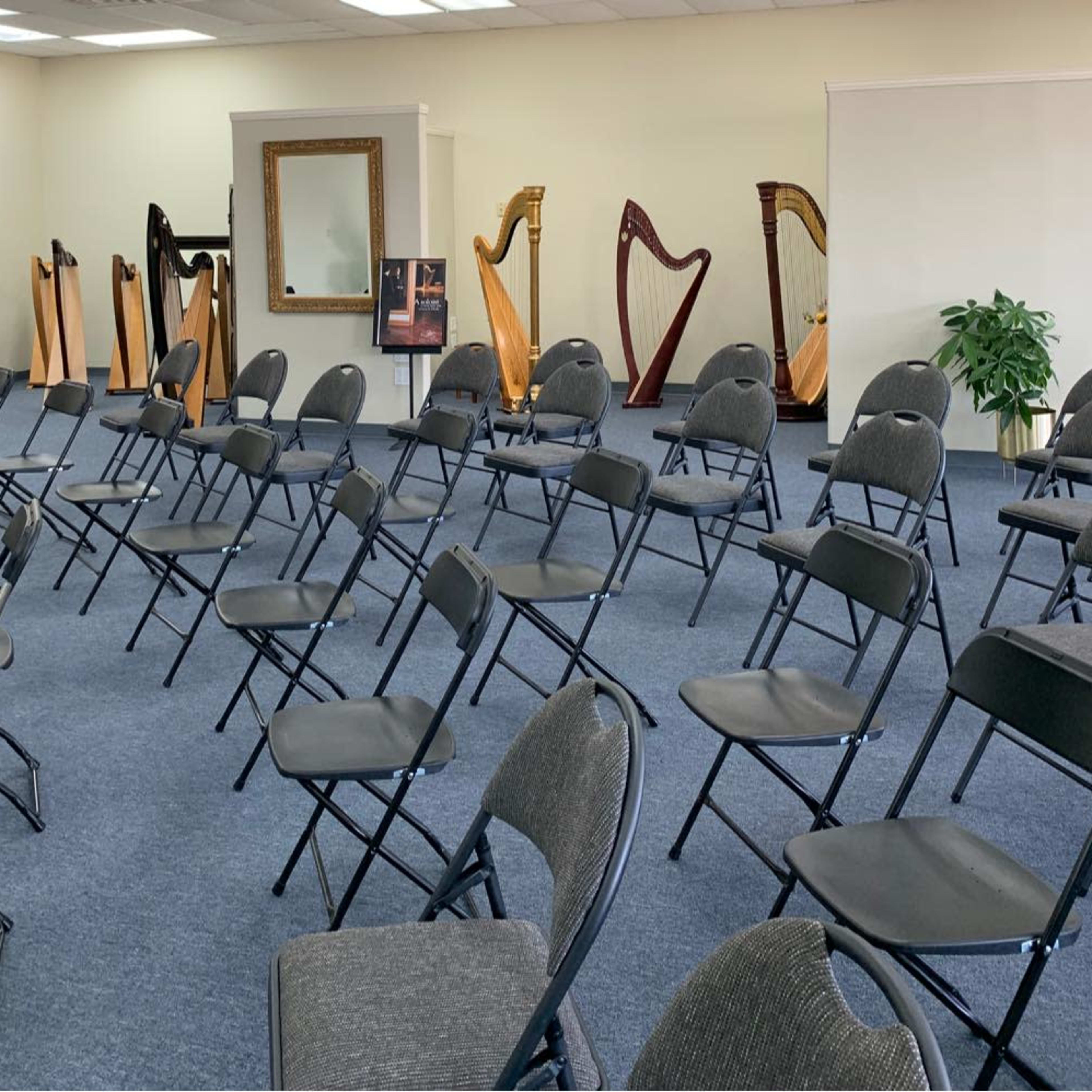 A room filled with folding chairs arranged in rows, facing several wooden harps displayed in the background.