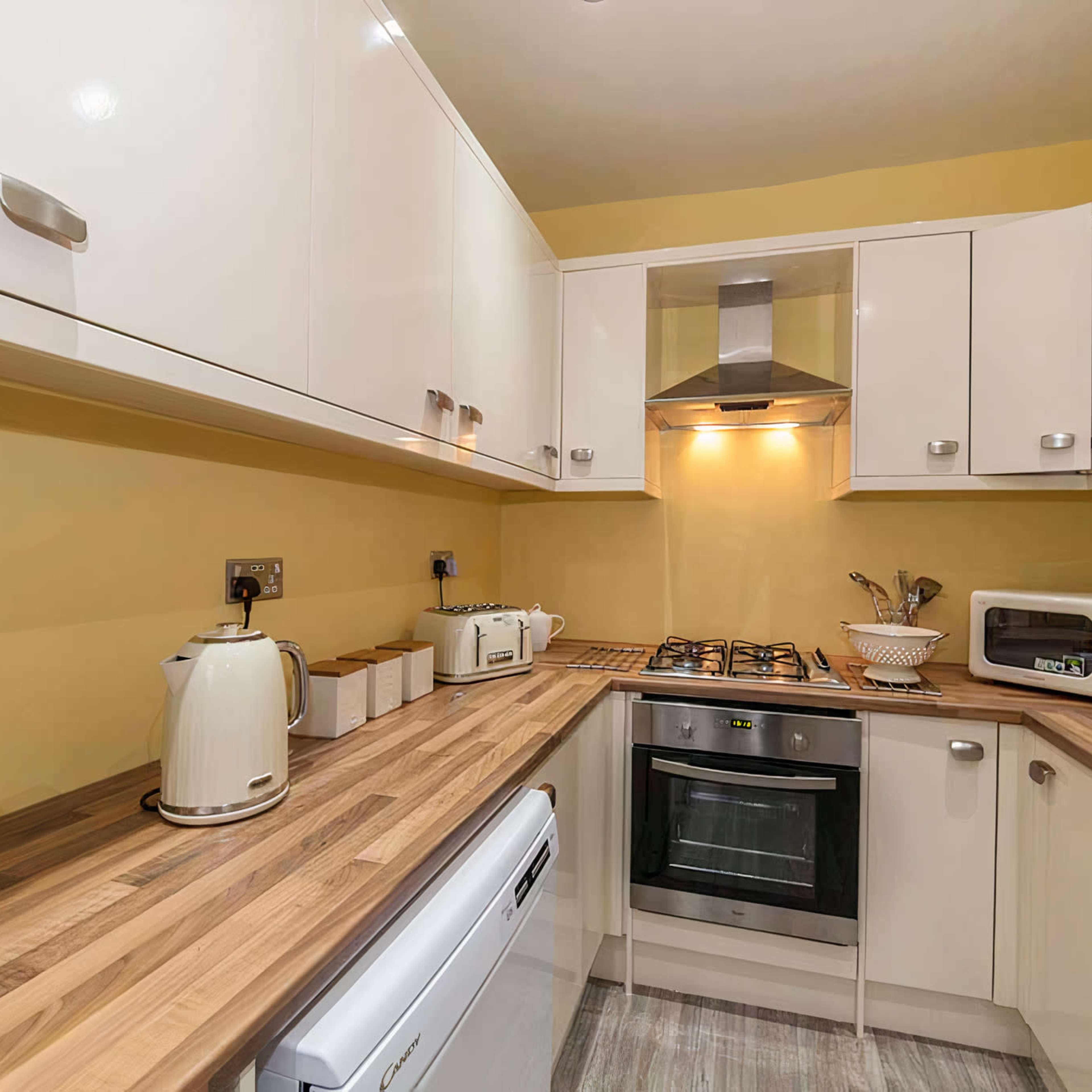 A small kitchen features white cabinets, a gas stove, and various appliances on a wooden countertop.