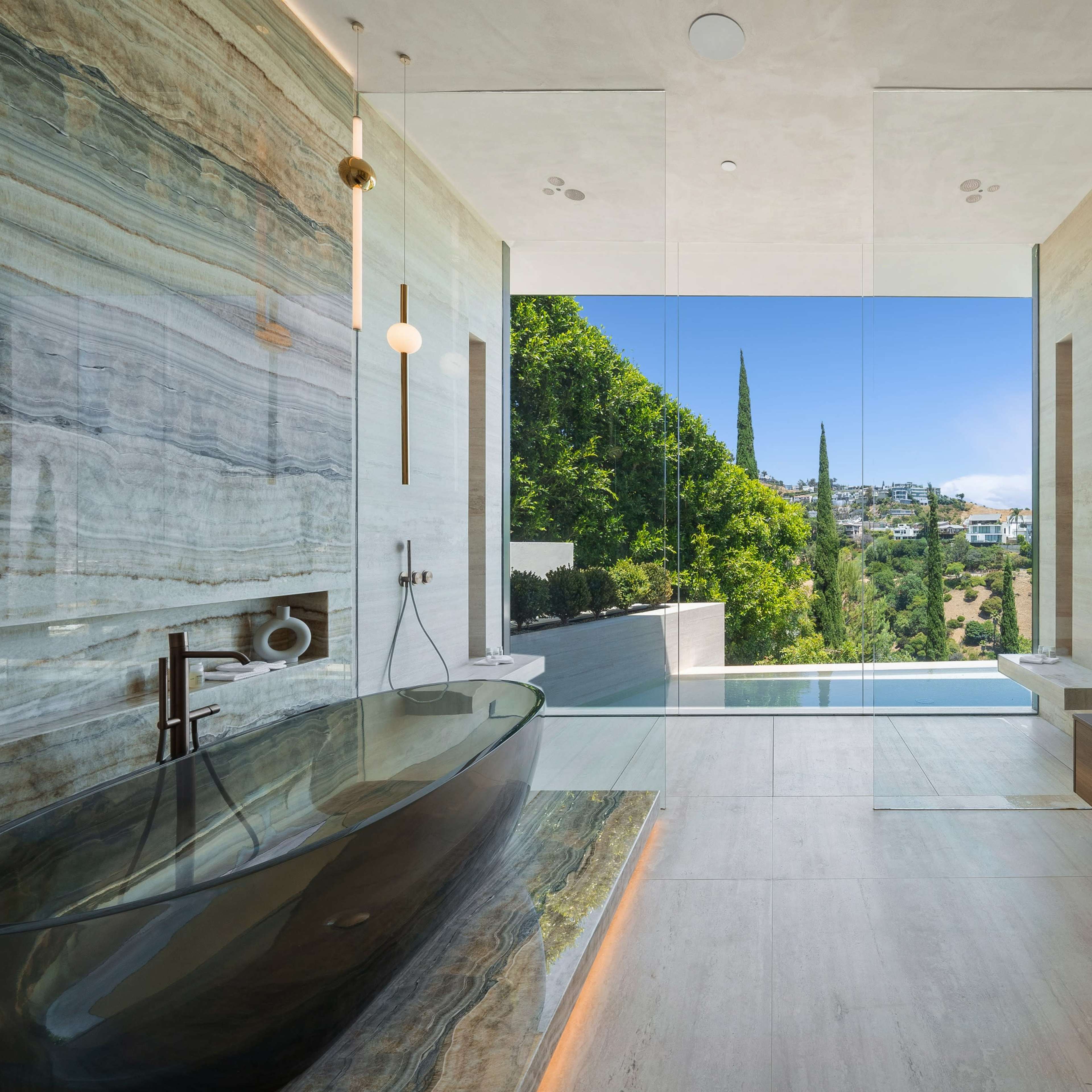 A modern bathroom with a large freestanding bathtub, a wooden vanity, and a scenic window overlooking greenery.