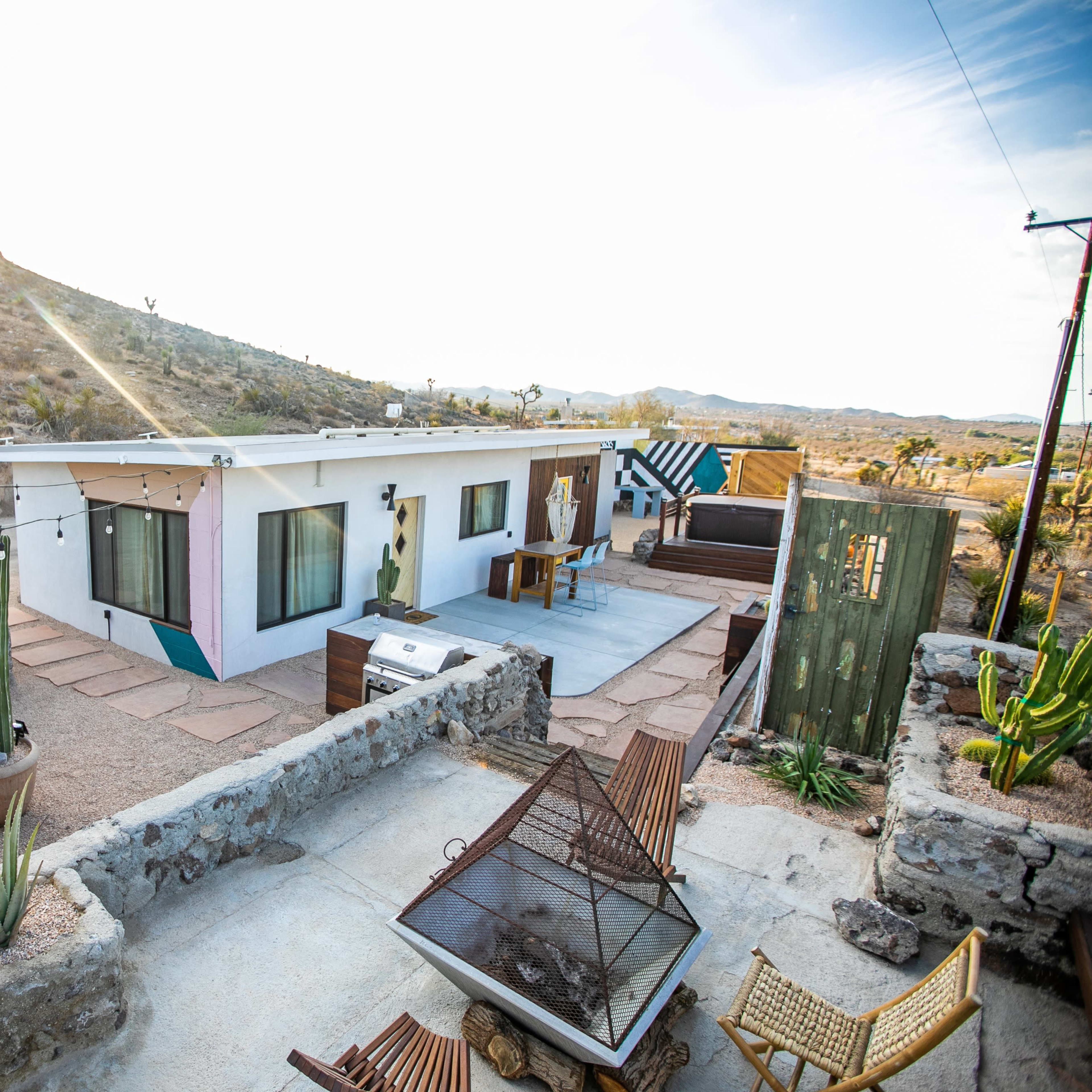 A modern house with a flat roof surrounded by desert terrain, featuring a patio area and various desert plants.