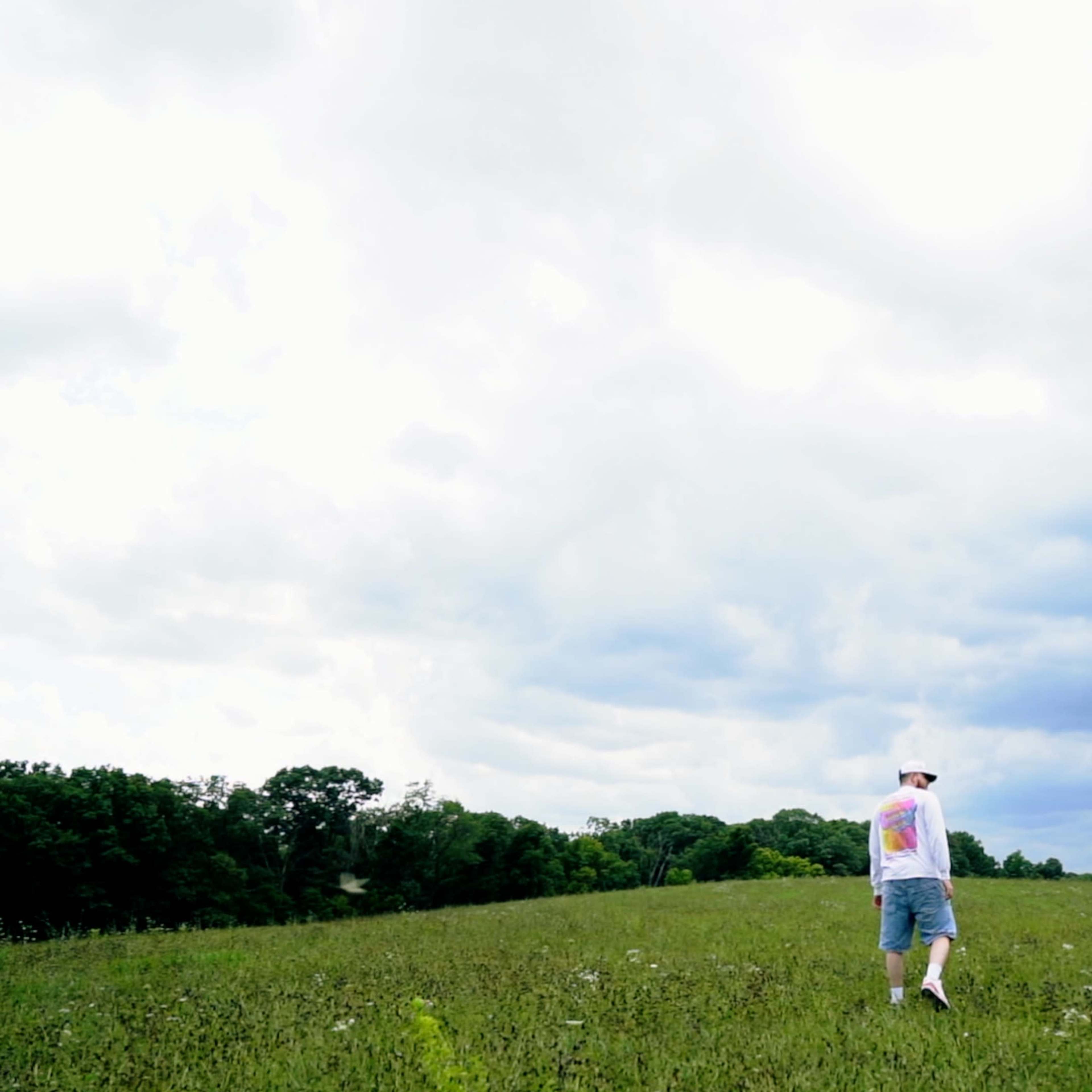 A person walks through a field under a cloudy sky.