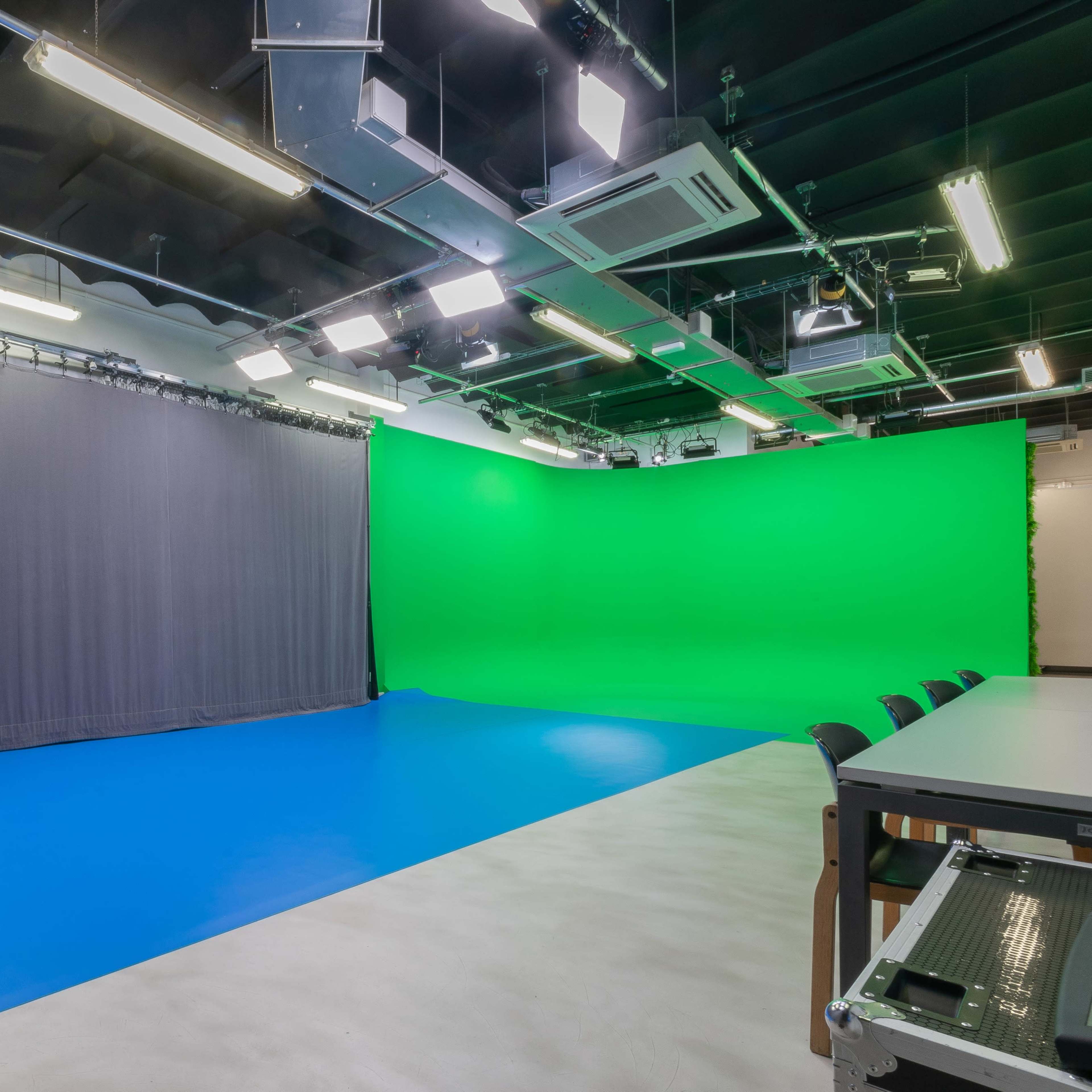 A studio with a green backdrop, gray drapes, and a blue floor, equipped with overhead lights.