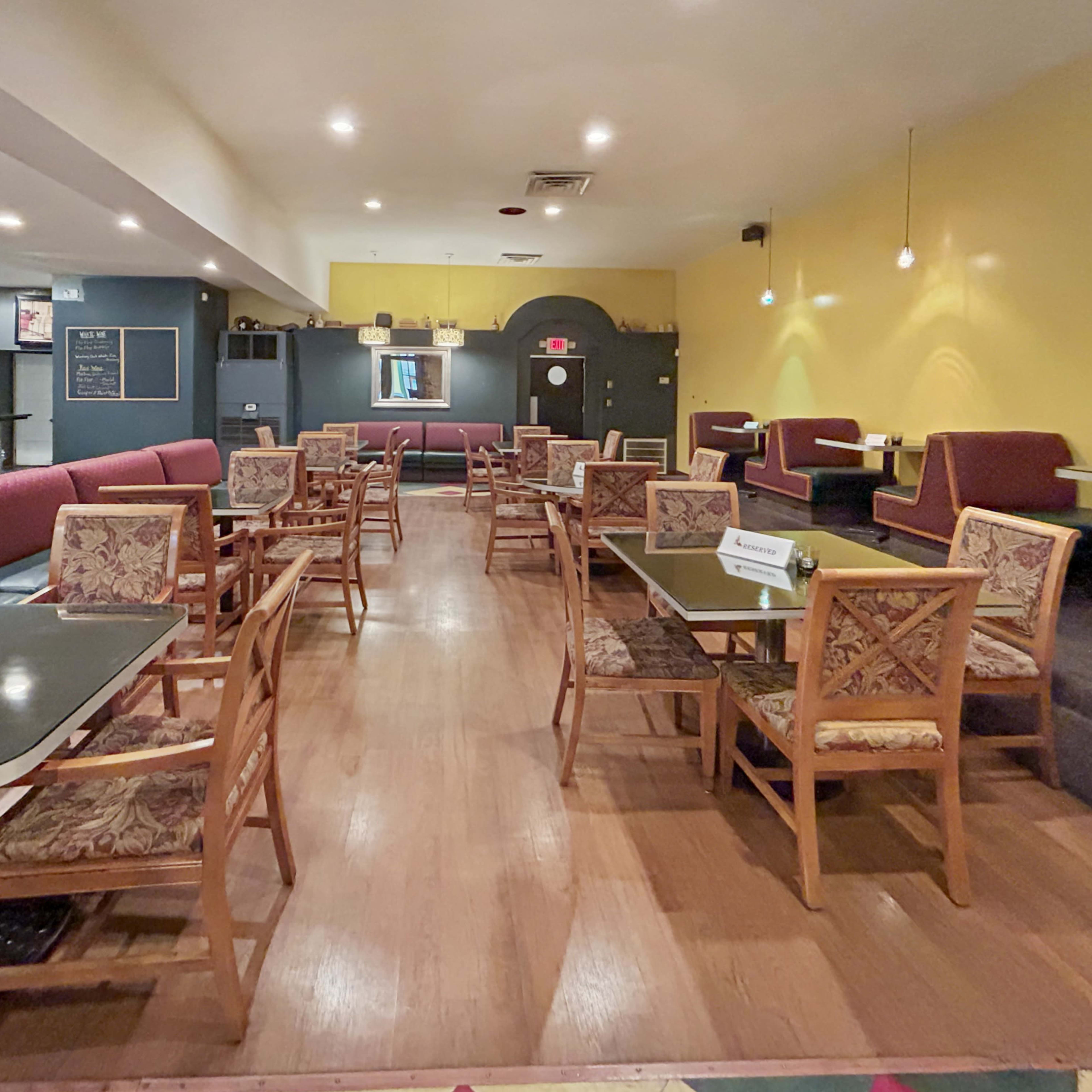 An interior view of a restaurant features wooden tables and chairs arranged neatly in a spacious, brightly lit room with yellow and gray walls.