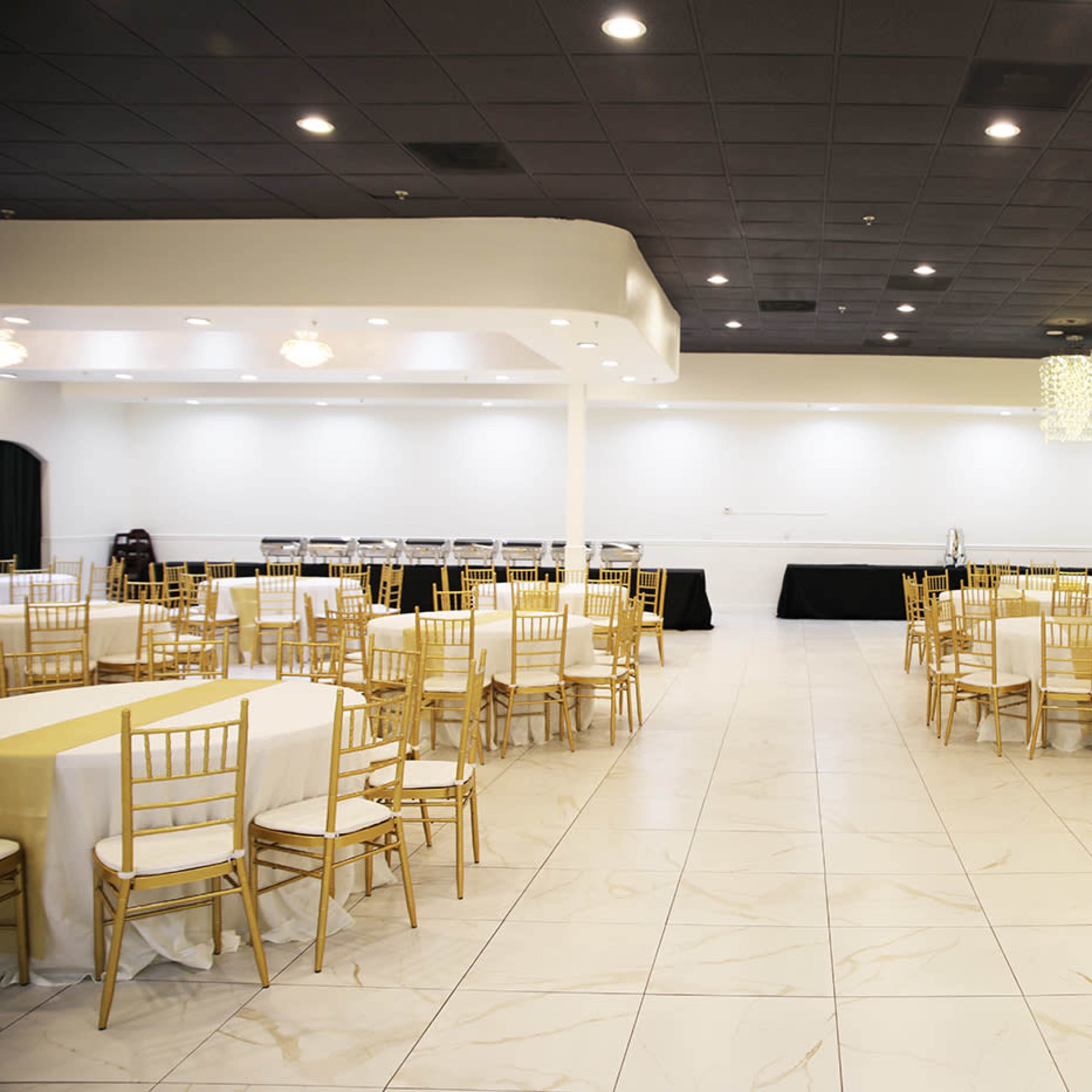 A large, empty banquet hall with gold chairs and tables arranged in a spacious layout.