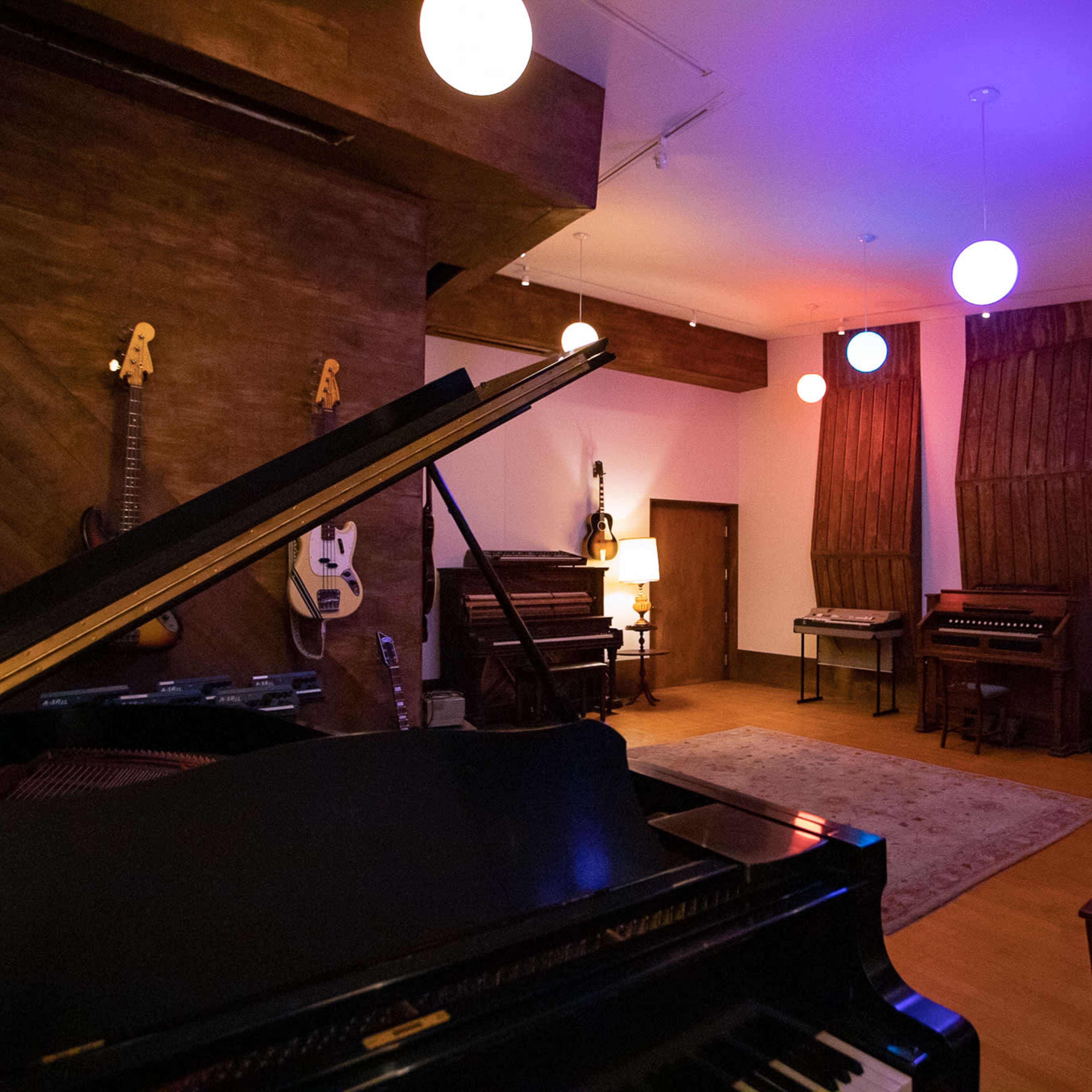 A spacious music studio featuring a grand piano, various instruments on display, and soft lighting from hanging orbs.