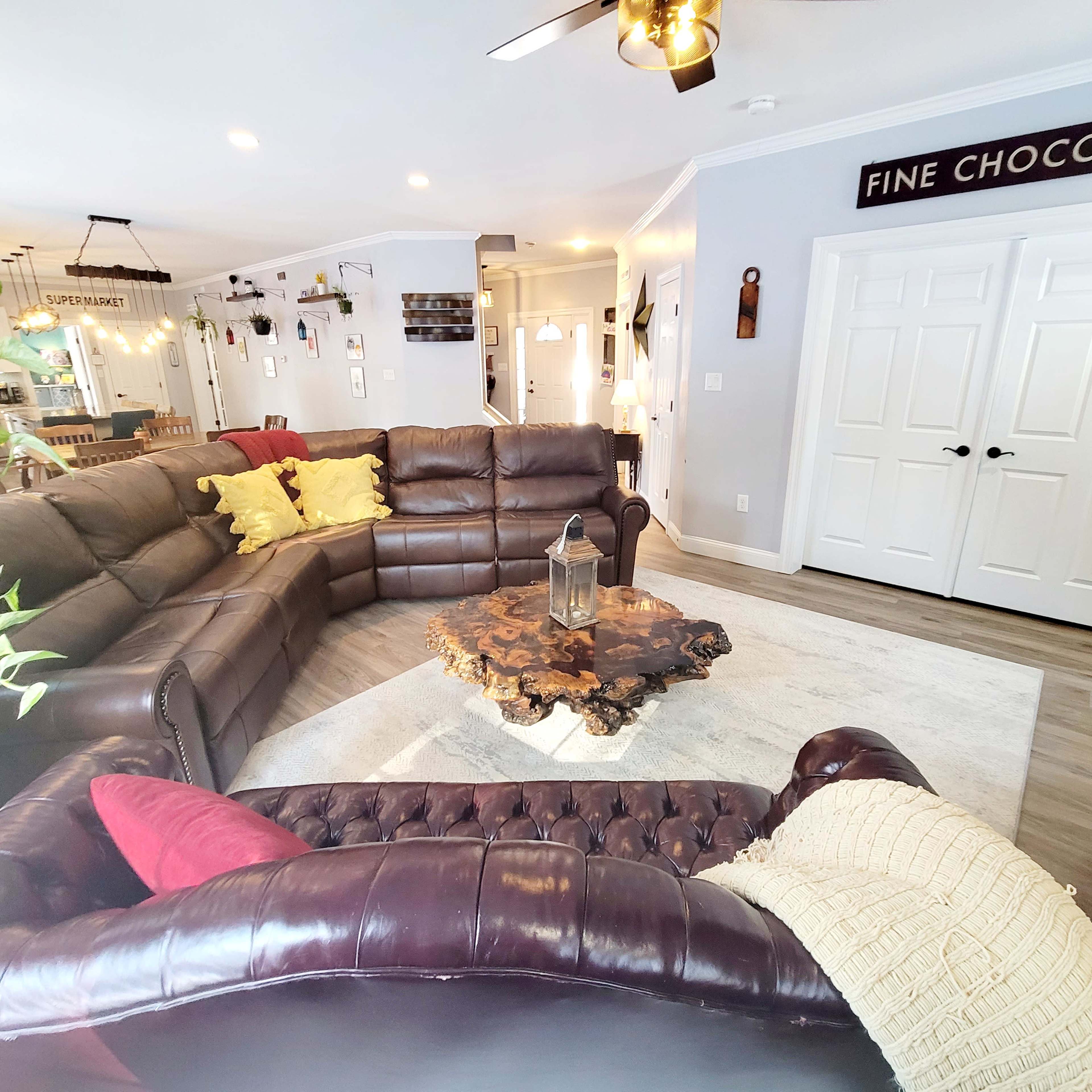 A spacious living room features a large brown leather sectional sofa, a wooden coffee table, and decorative plants.