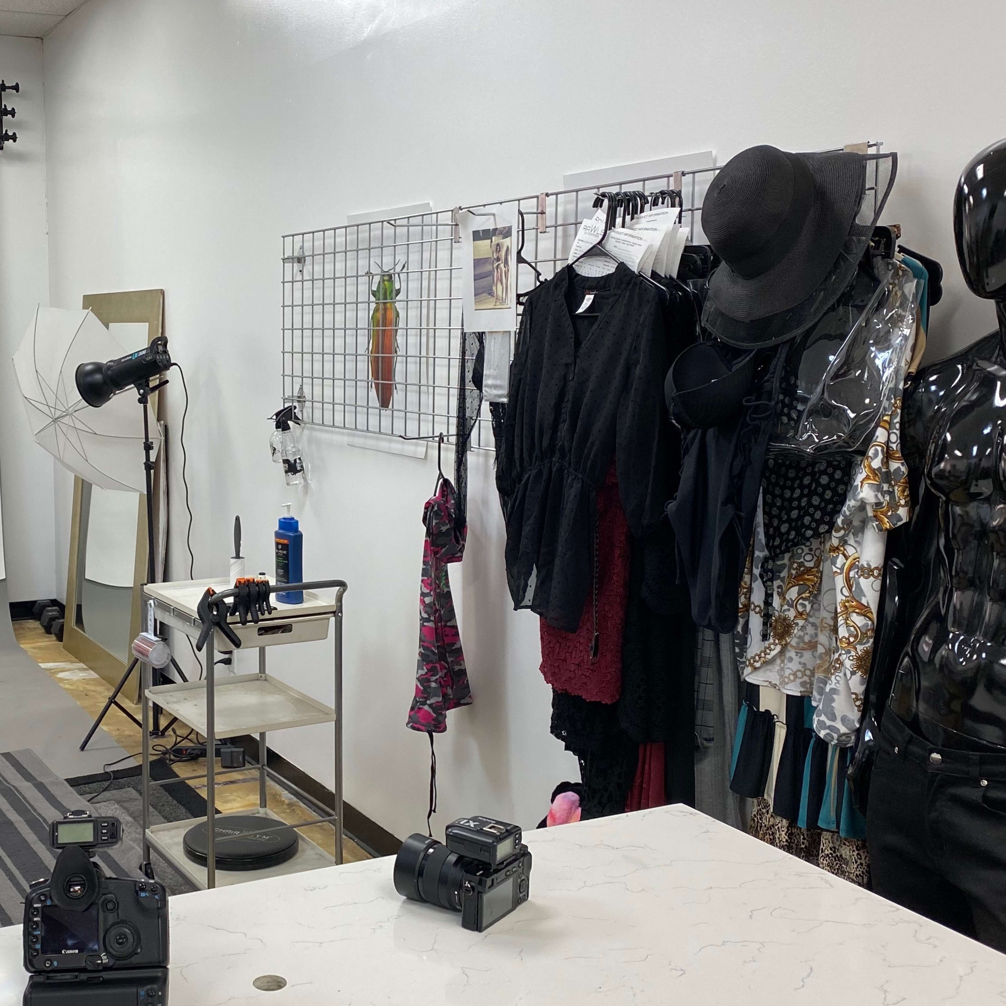 A photography studio features a backdrop, lighting equipment, and clothing displays alongside cameras on a table.