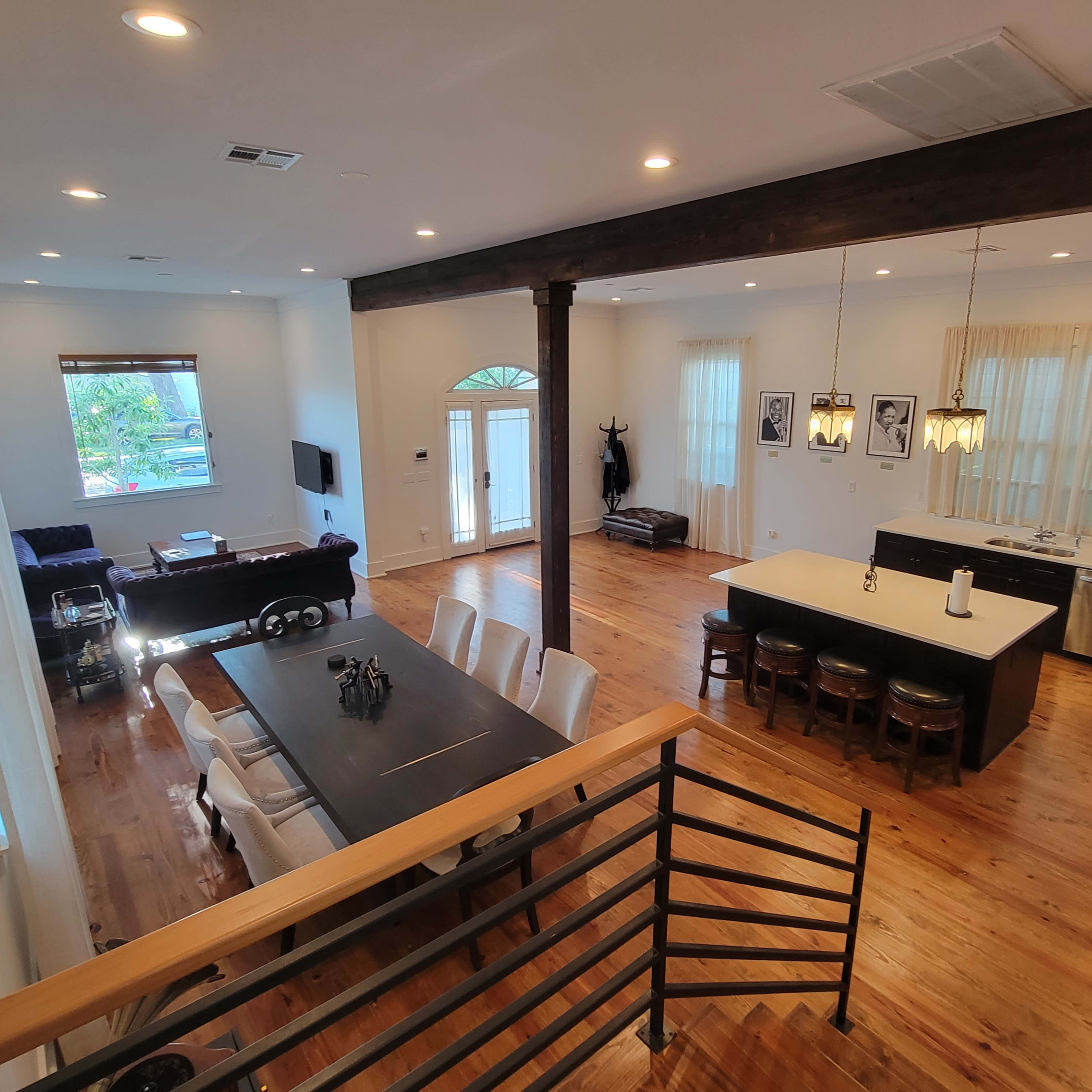 A bright, open-concept living space featuring a dining area with a long table, a kitchen island with stools, and a cozy seating area with a sofa.