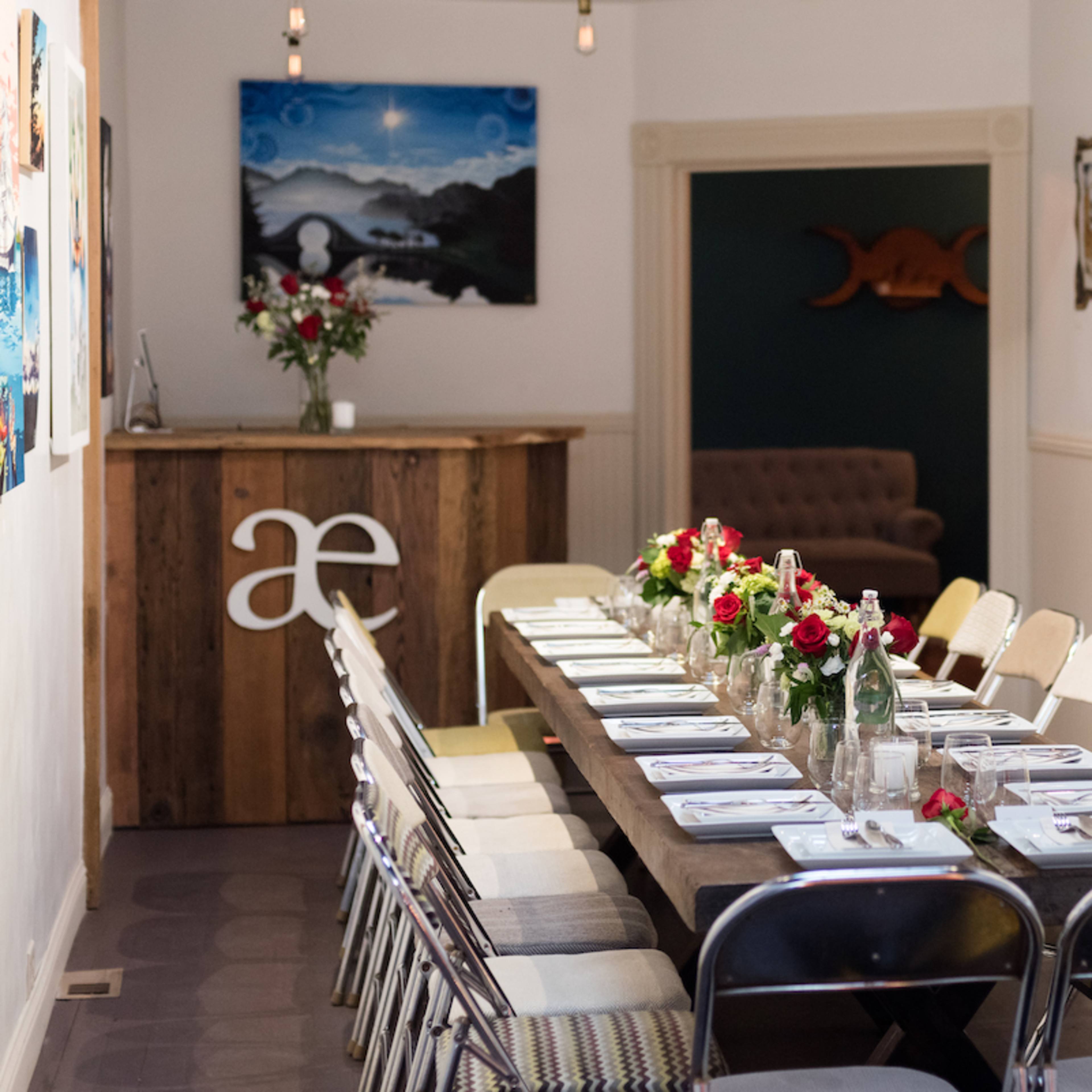 A long wooden table is set with plates and flowers in a brightly lit room featuring artwork on the walls.